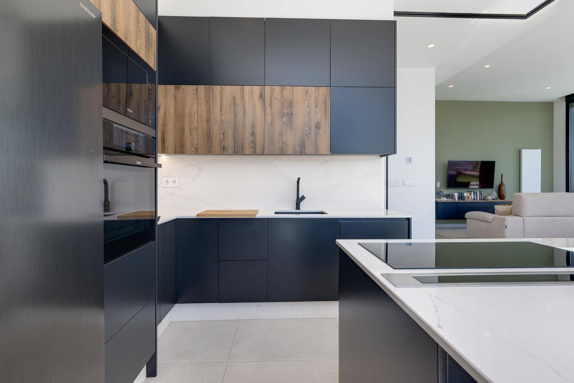 Moderne offene Küche mit dunklen Schränken, Holzdetails und heller Arbeitsplatte, integriertem Backofen und Mikrowelle.