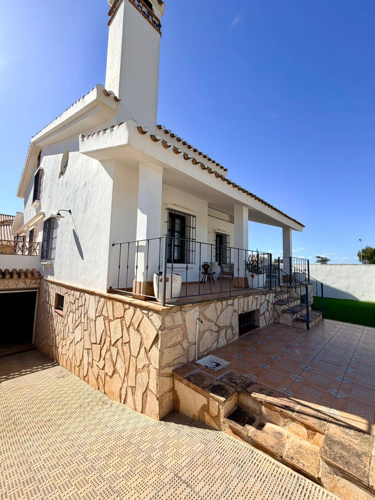 Seitenansicht der Villa mit gepflasterter Auffahrt, Steinfassade und Zugang zur Terrasse.