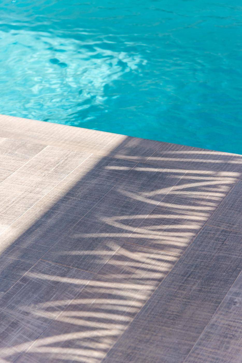 Nahaufnahme des Pools mit klarem Wasser und Sonnenlicht, das Schatten auf die Terrasse wirft.