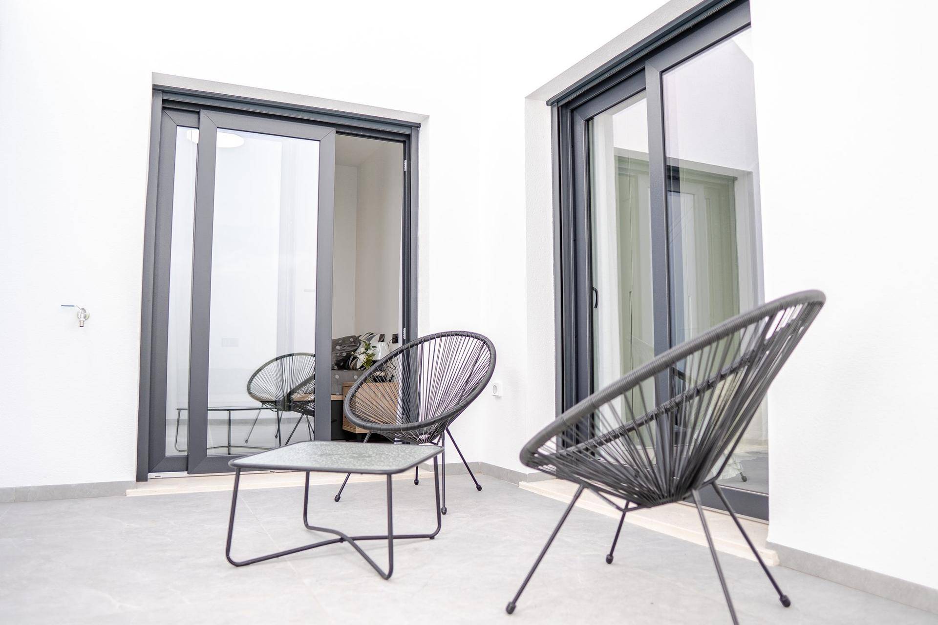 Moderne Terrasse mit schwarzen Outdoor-Sesseln und Schiebetüren zum Innenbereich des Hauses.