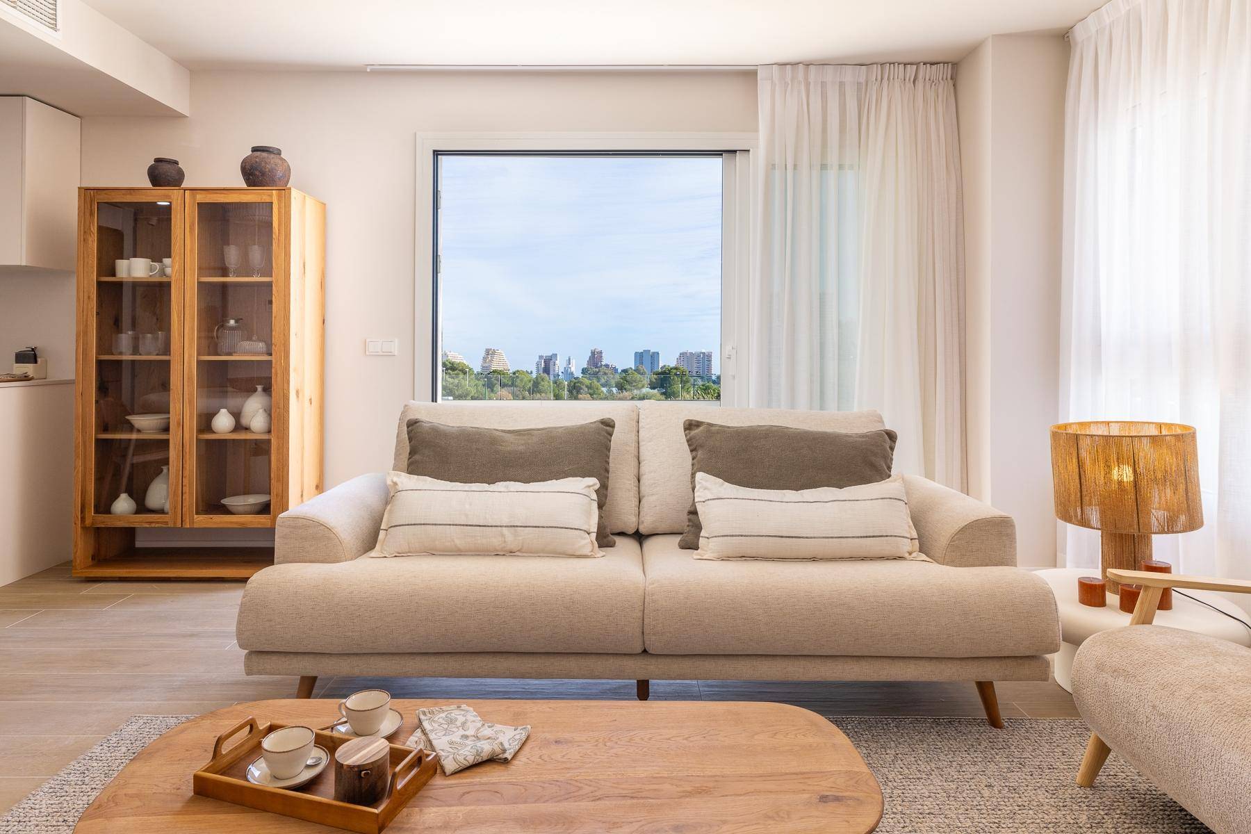 Helles Wohnzimmer mit beigem Sofa, Holztisch und Stadtblick durch das große Fenster.