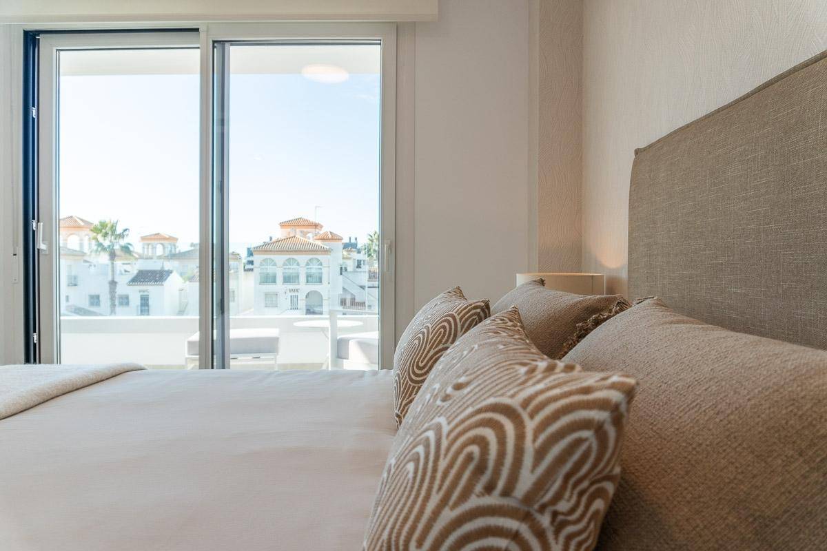 Helles Schlafzimmer mit Doppelbett und großen Schiebetüren, die zu einem Balkon führen.