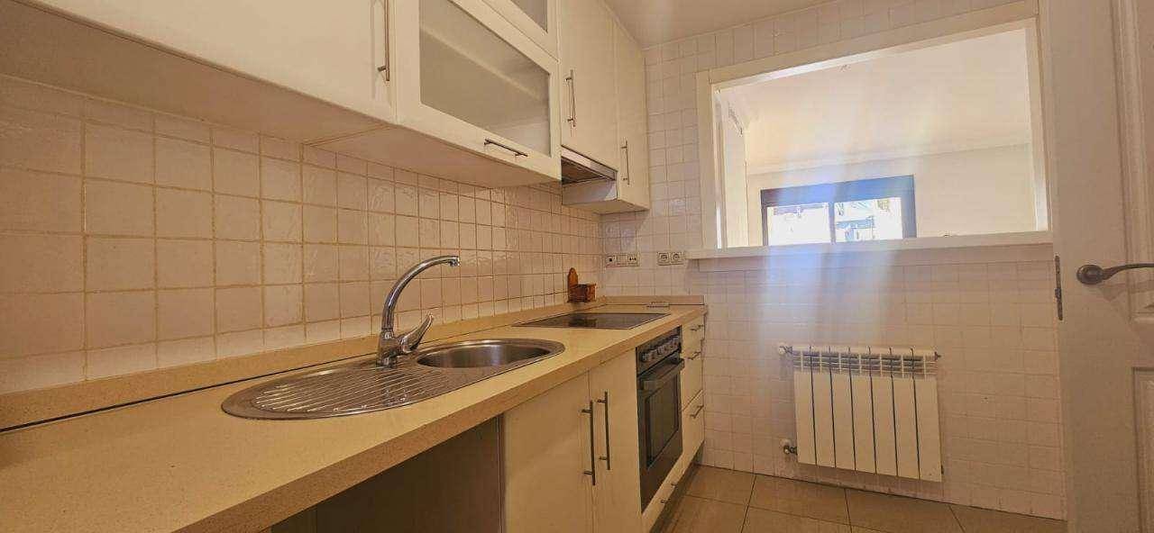 Helle Küche mit weißen Oberschränken, integriertem Ofen und Heizkörper unter dem Fenster.