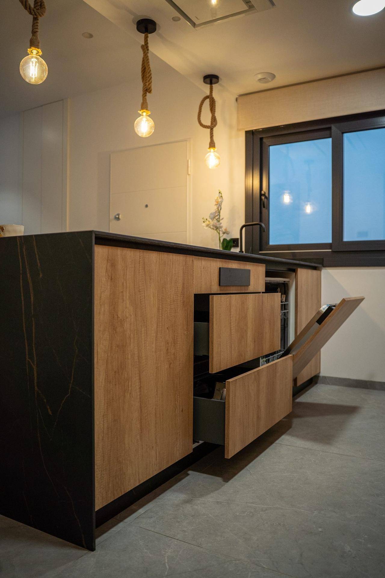Moderne Kücheninsel mit dunkler Arbeitsplatte, Holzfronten und einzigartigen Seil-Pendelleuchten.