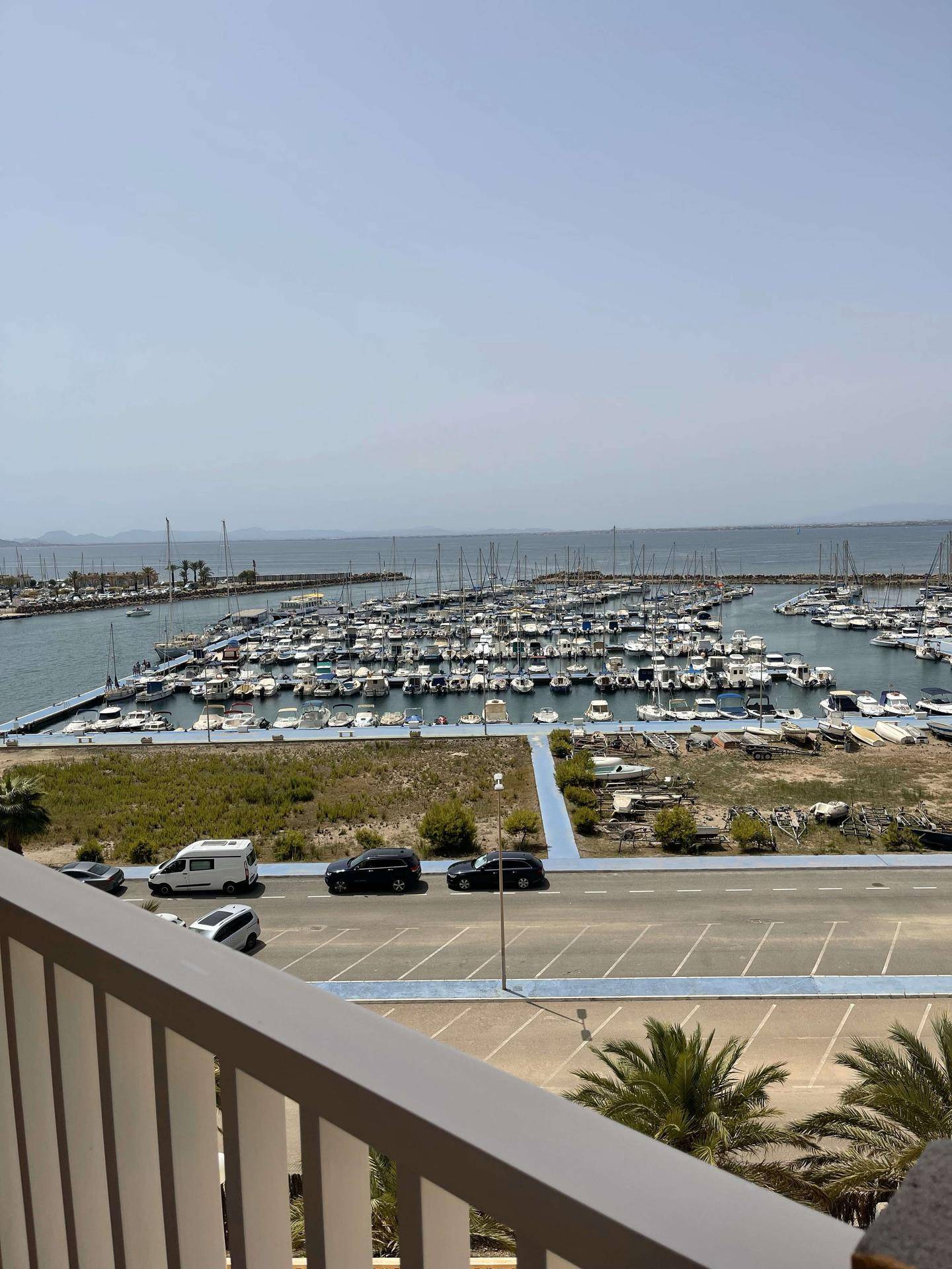 Balkon mit Blick auf den belebten Yachthafen und das weite Meer unter klarem Himmel.