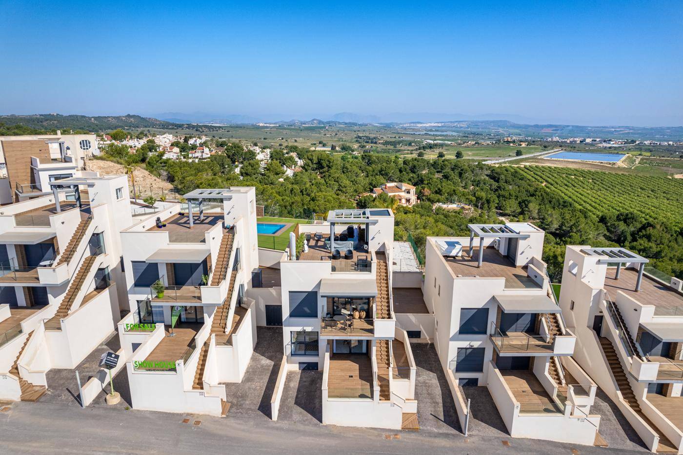Moderne Reihenhäuser mit Terrassen und Pools, umgeben von grüner Landschaft.