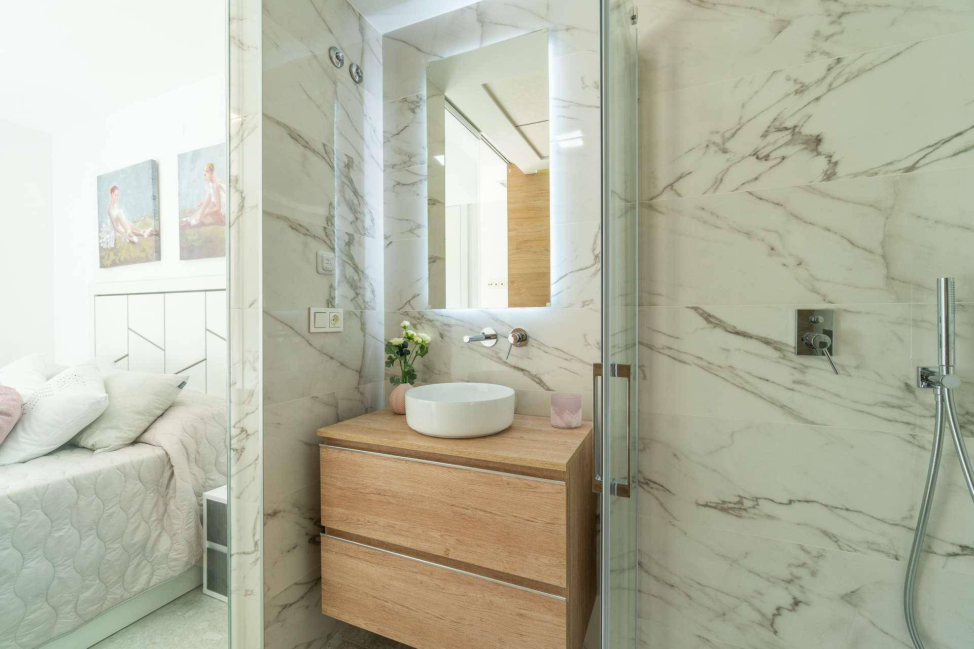 Modernes Badezimmer mit stilvollem Waschtisch, beleuchtetem Spiegel und Blick ins Schlafzimmer.