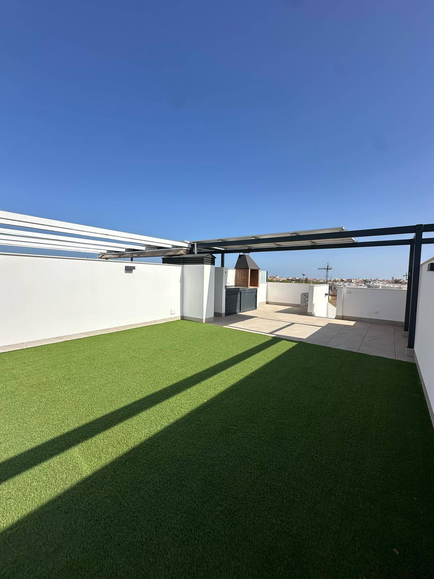 Weitläufige Dachterrasse mit Kunstrasen, Grillbereich und Solarpaneelen unter blauem Himmel.