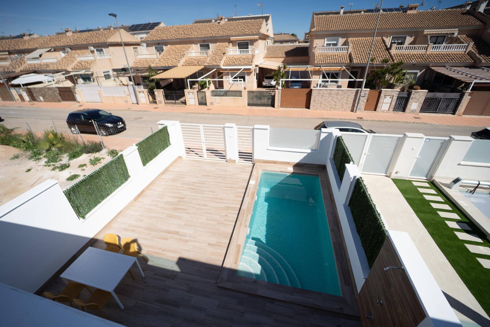 Sonniger Außenbereich mit privatem Pool, Holzdeck und Sitzgelegenheiten vor Reihenhäusern.