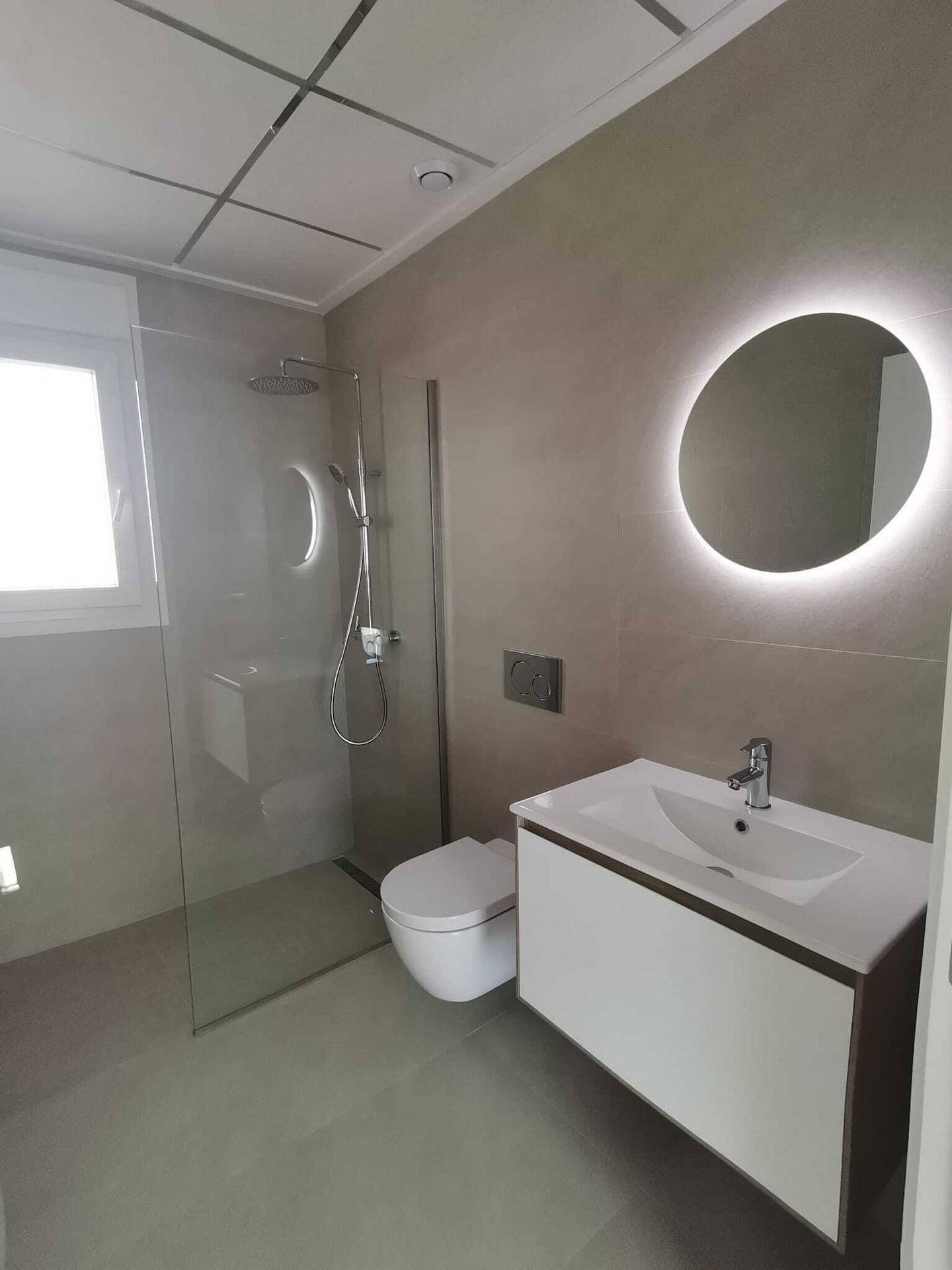 Modernes Badezimmer mit begehbarer Dusche, schwebendem Waschtisch und beleuchtetem Spiegel.