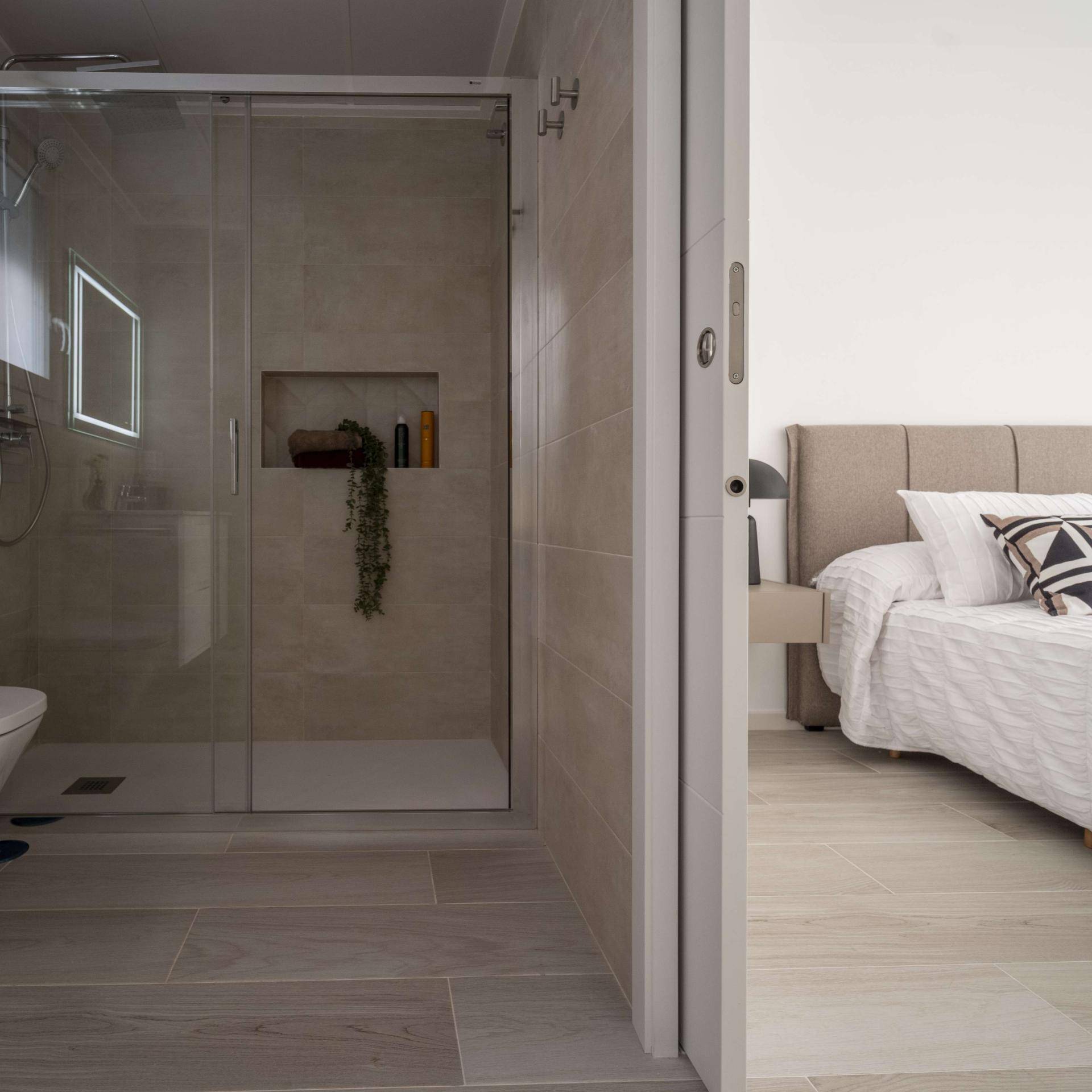 Helles Schlafzimmer mit direktem Zugang zu einem modernen Badezimmer mit Dusche.