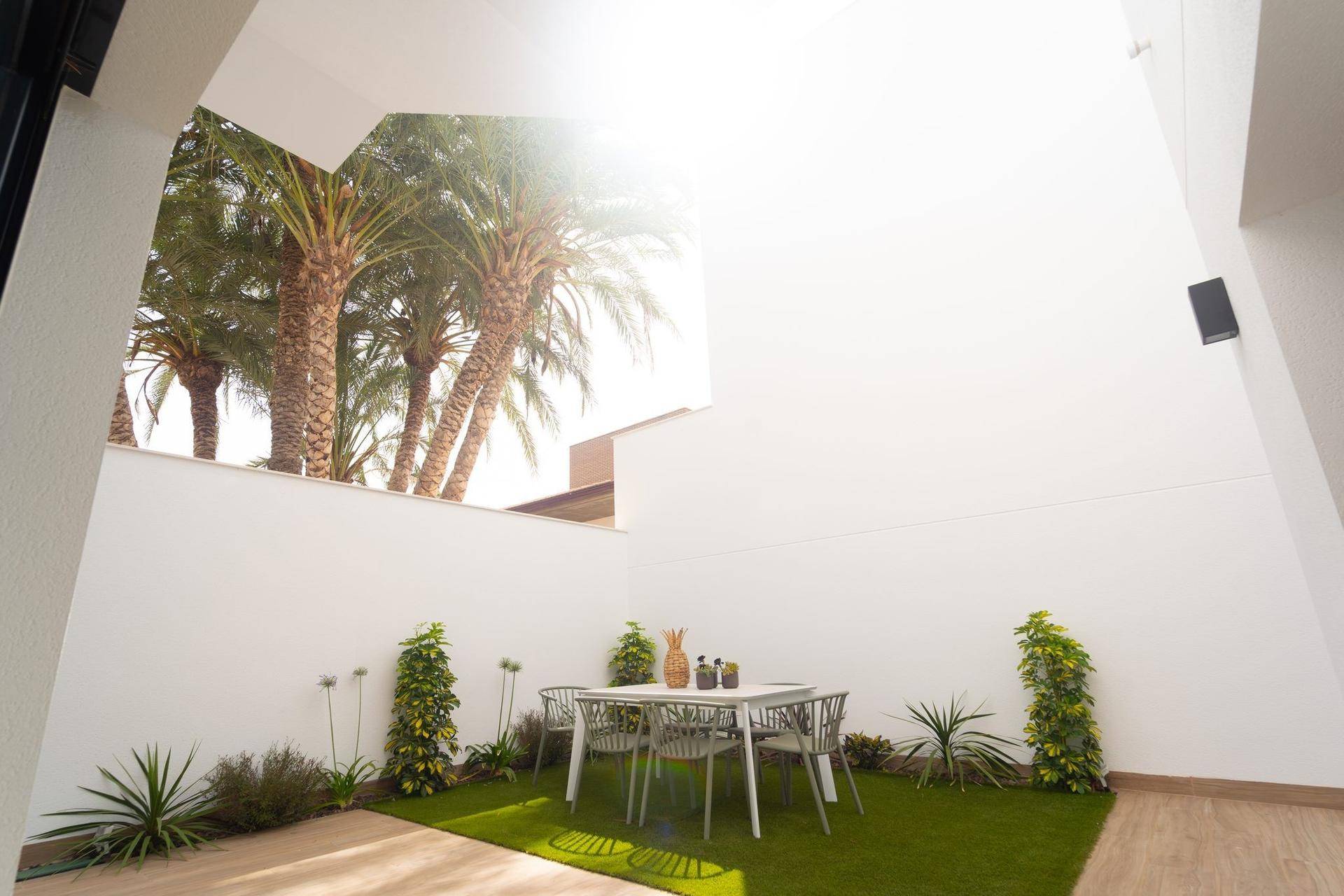 Heller Gartenbereich mit Kunstrasen, Esstisch und Palmen im Hintergrund, perfekt zum Entspannen.