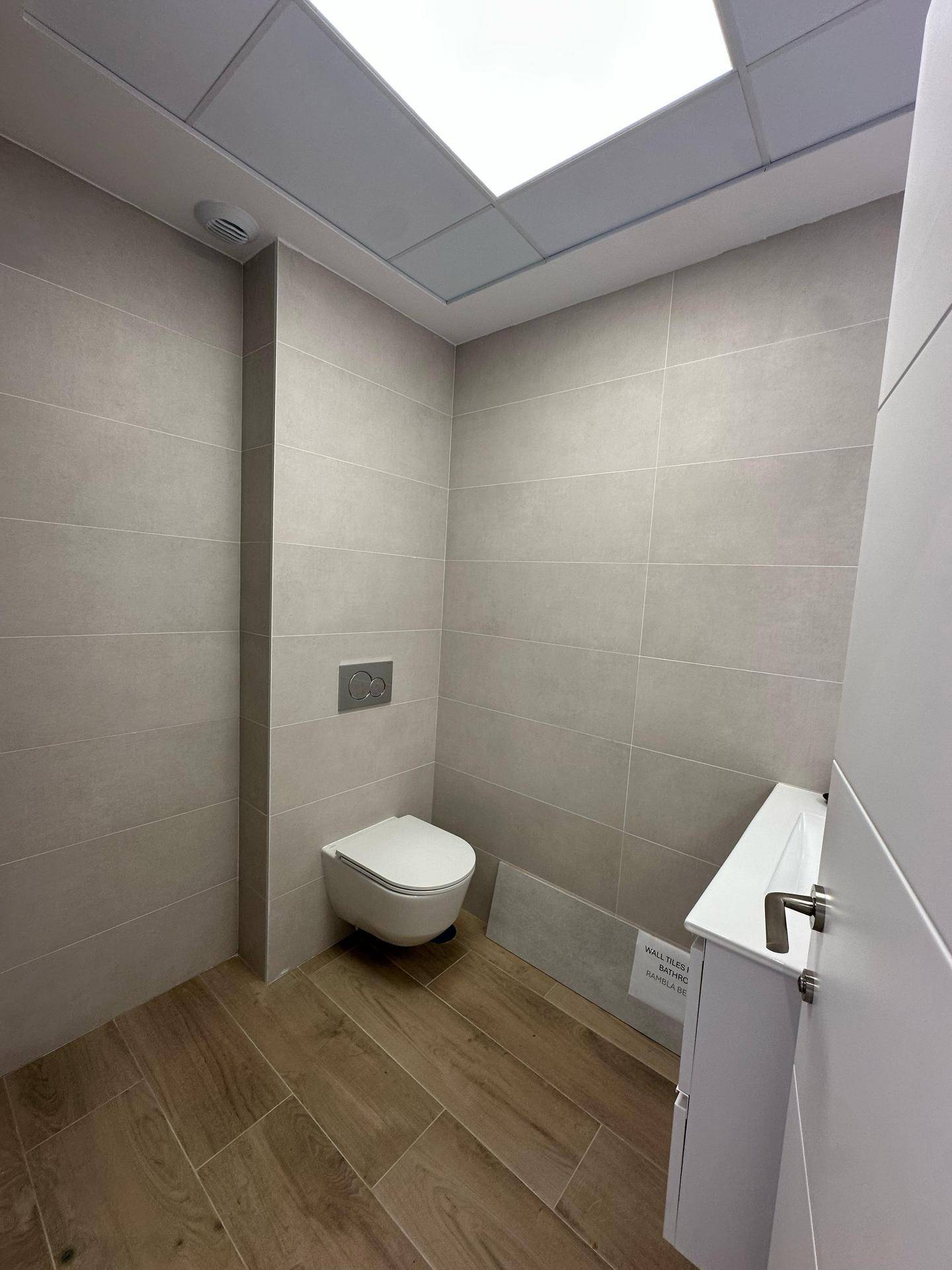 Modernes WC mit wandhängender Toilette und hellen Fliesen an den Wänden.