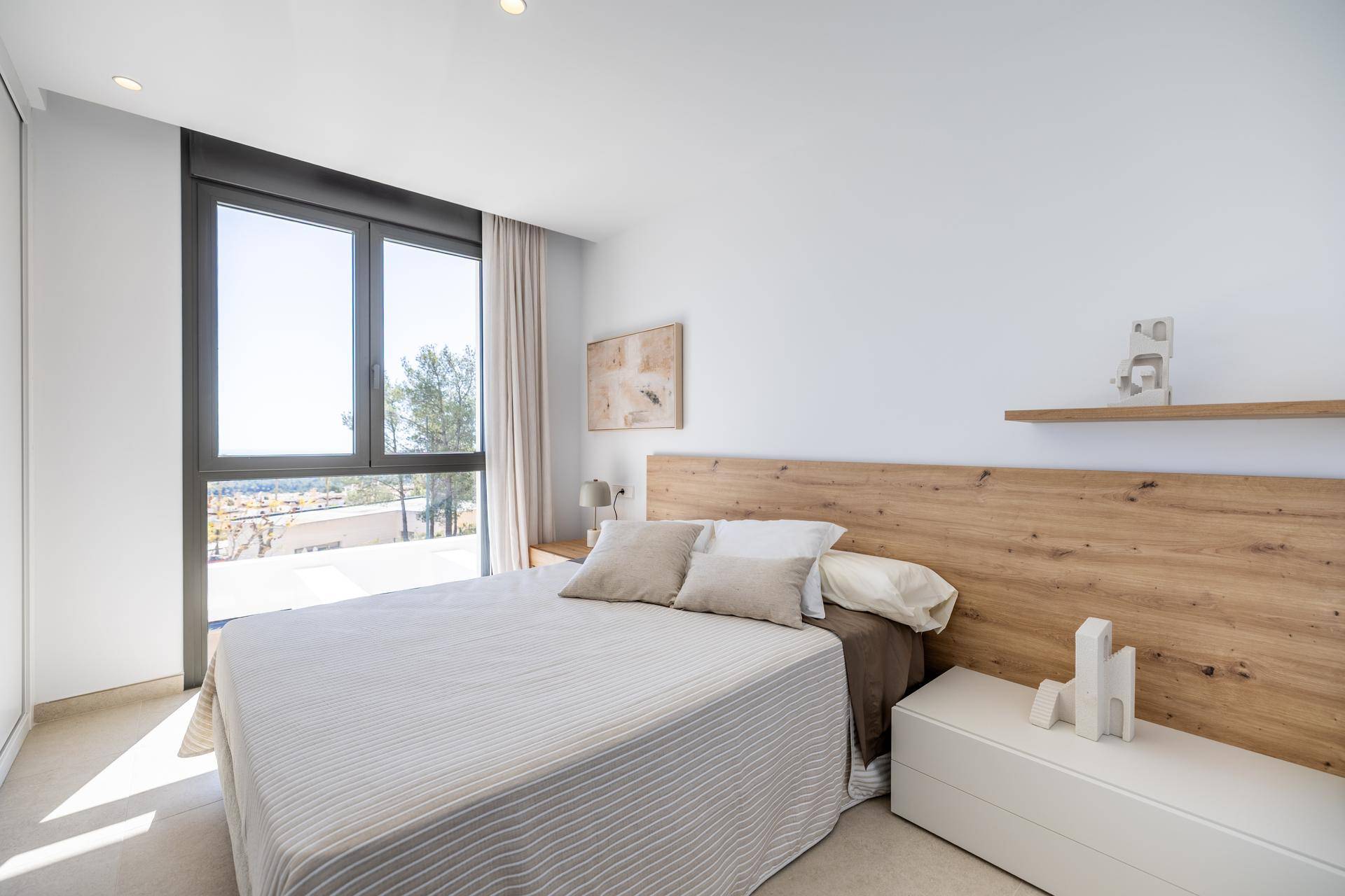 Helles Schlafzimmer mit Holzkopfteil, schwebendem Regal und großem Fenster mit Ausblick.