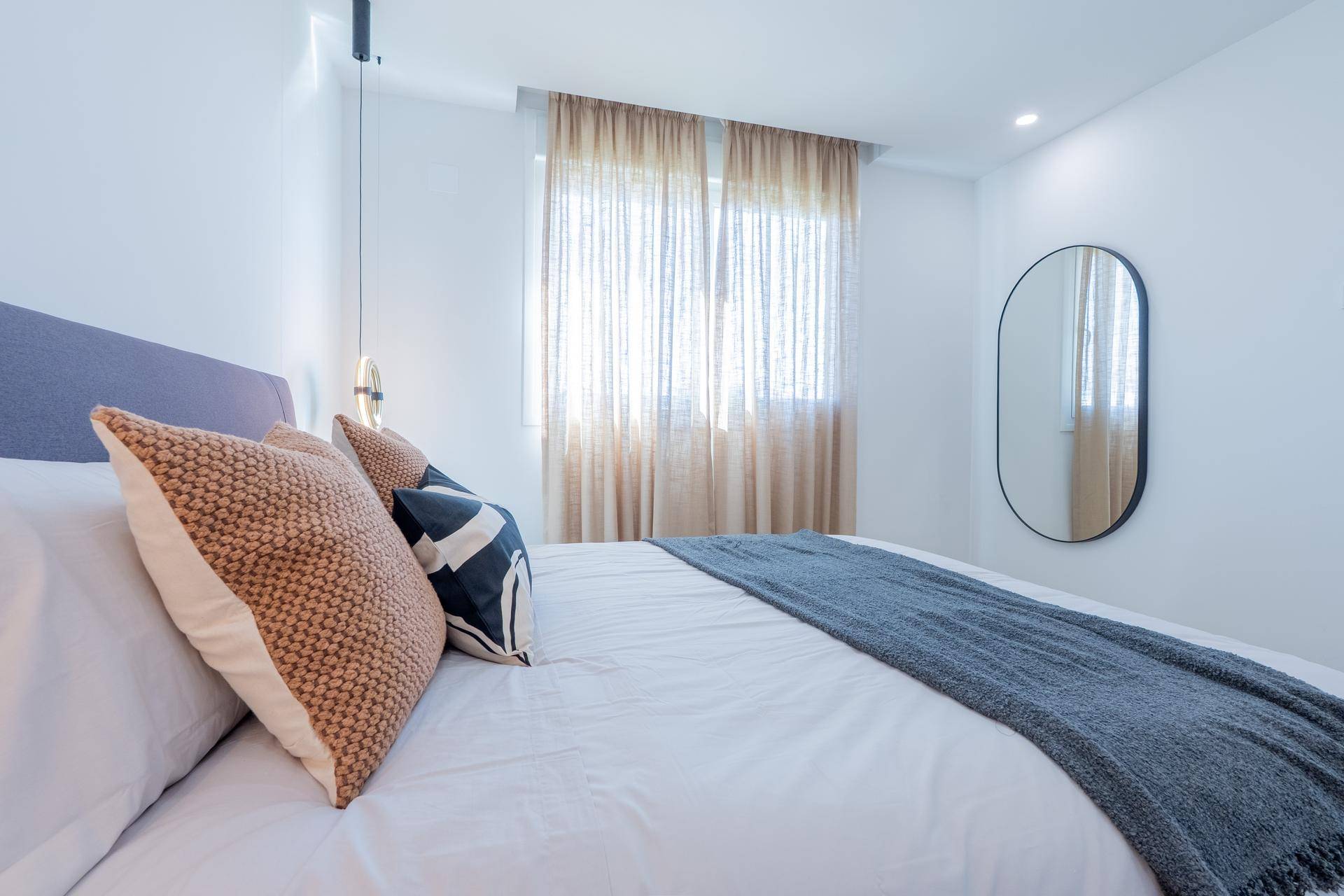 Helles Schlafzimmer mit Doppelbett, modernen Nachttischlampen und Vorhängen am Fenster.