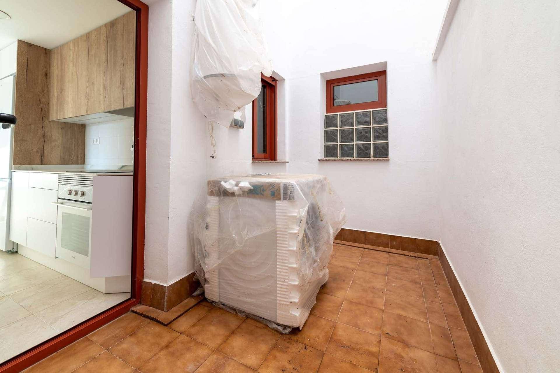 Kleiner Hauswirtschaftsraum mit Fliesenboden, Fenster und einem verpackten Gerät.