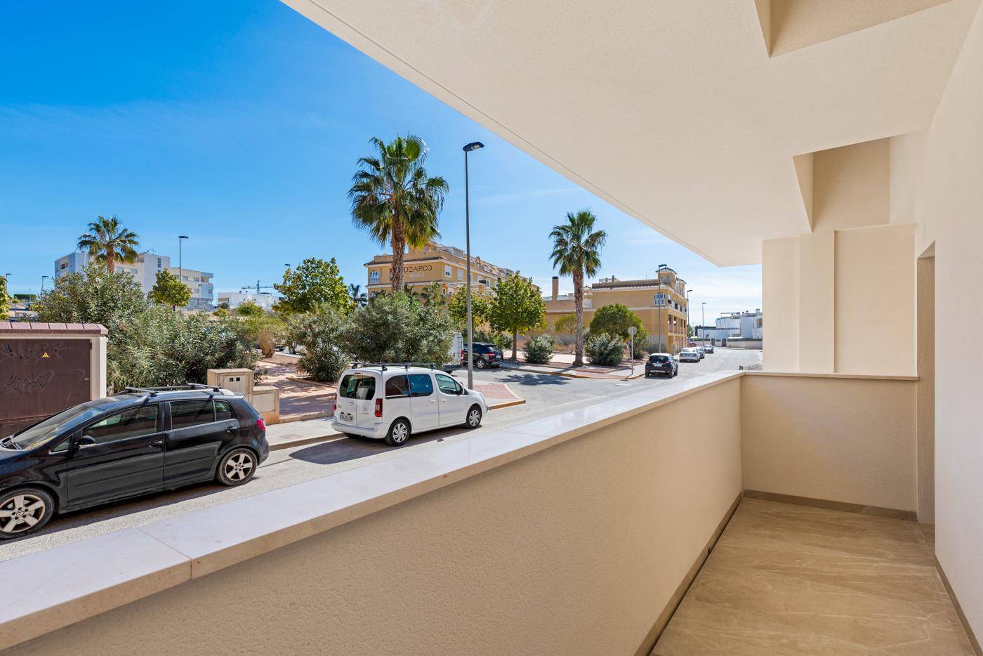 Heller Balkon mit Fliesenboden und Blick auf die Straße mit Palmen.