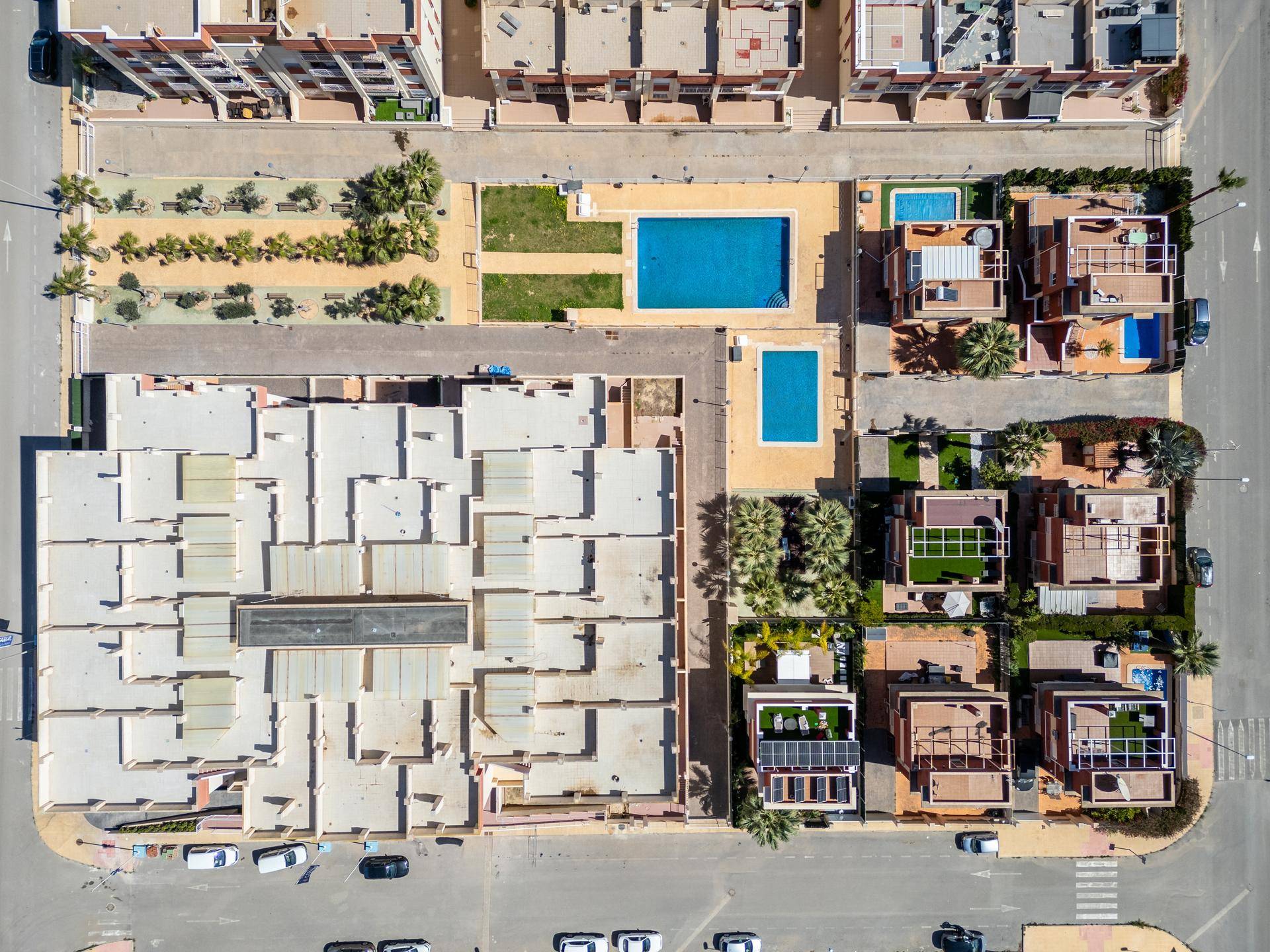 Vogelperspektive des Wohnkomplexes mit Flachdächern, zwei Pools und der umliegenden Infrastruktur.