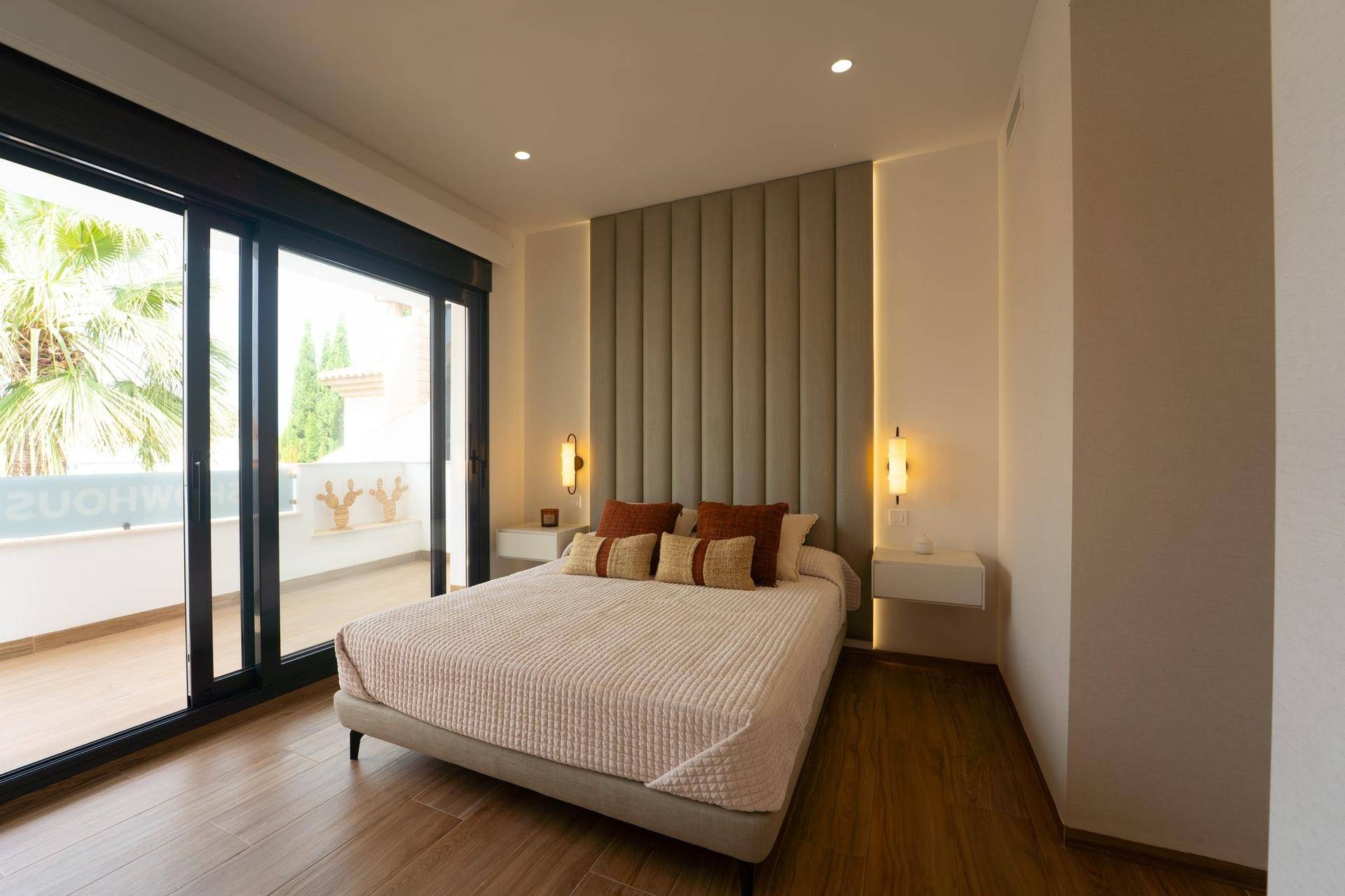 Modernes Schlafzimmer mit großem Bett, gepolstertem Kopfteil und Zugang zum Balkon.
