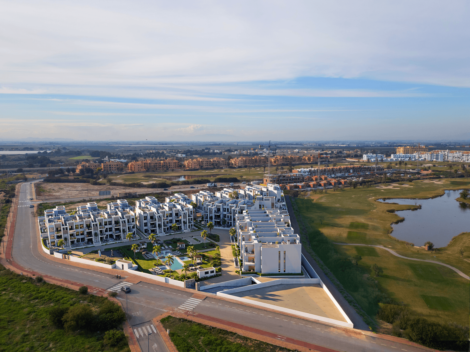 Weitläufige Luftaufnahme einer modernen Wohnanlage mit Golfplatz, See und umliegender Landschaft.