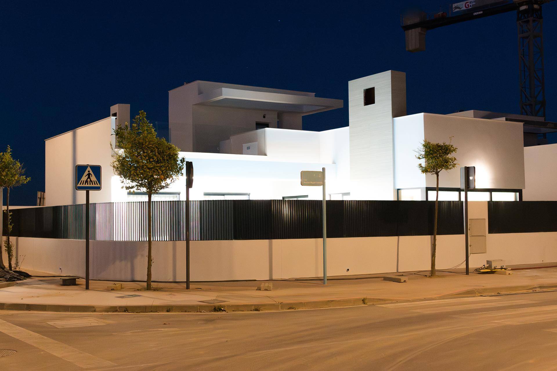Moderne Villa von der Straße aus bei Nacht beleuchtet, mit klaren Linien und Zaun.