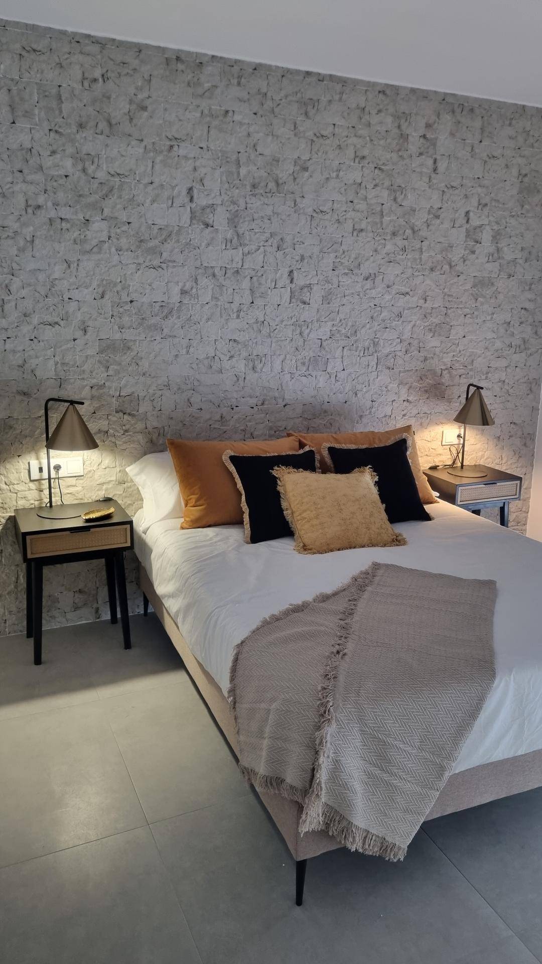 Schlafzimmer mit dekorativer Steinwand, Doppelbett und Nachttischen mit Lampen.