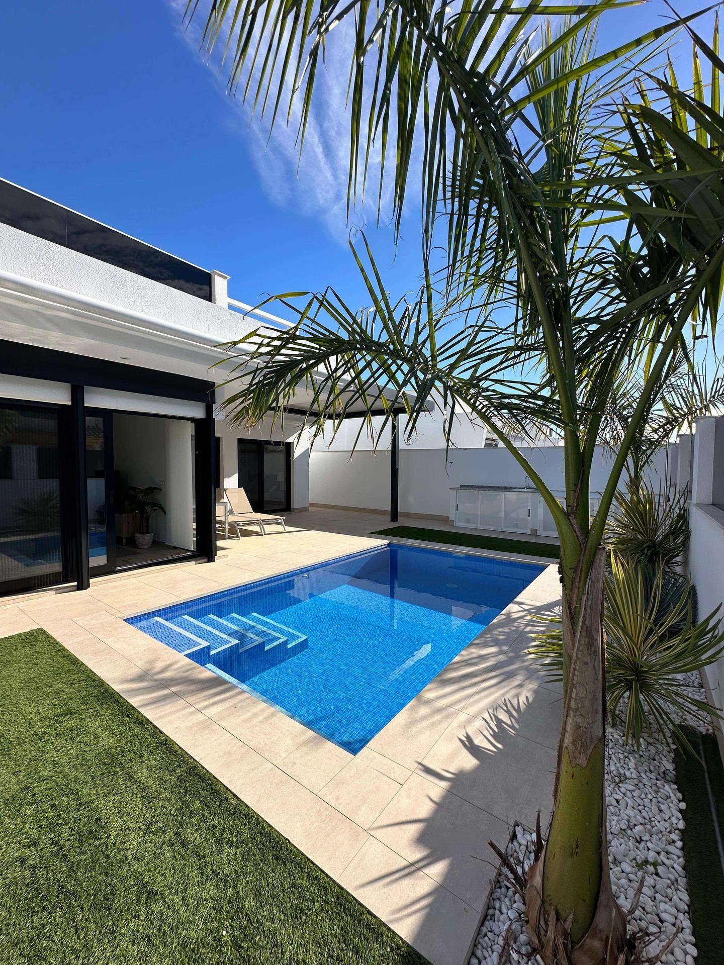Sonniger Gartenbereich mit Pool, Palmen und weißem Kies, der zum Entspannen einlädt.