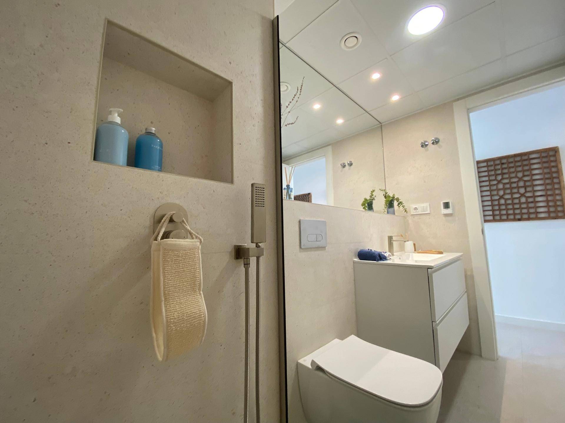 Modernes Badezimmer mit wandhängendem WC, kleinem Waschtisch und praktischer Duschablage.