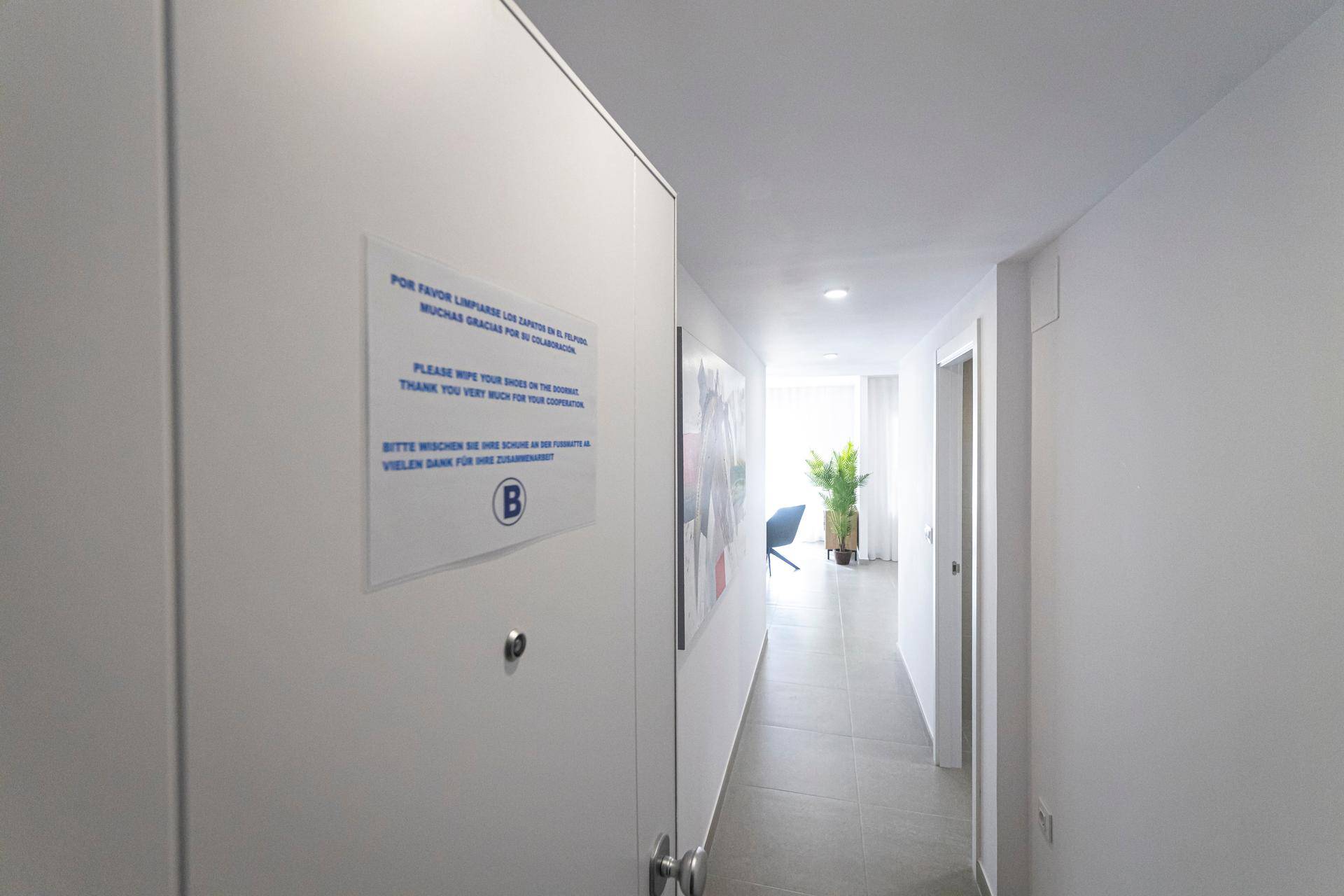 Heller Flur mit Fliesenboden und einer Notiz an der Wand, die zum Schuheputzen auffordert.