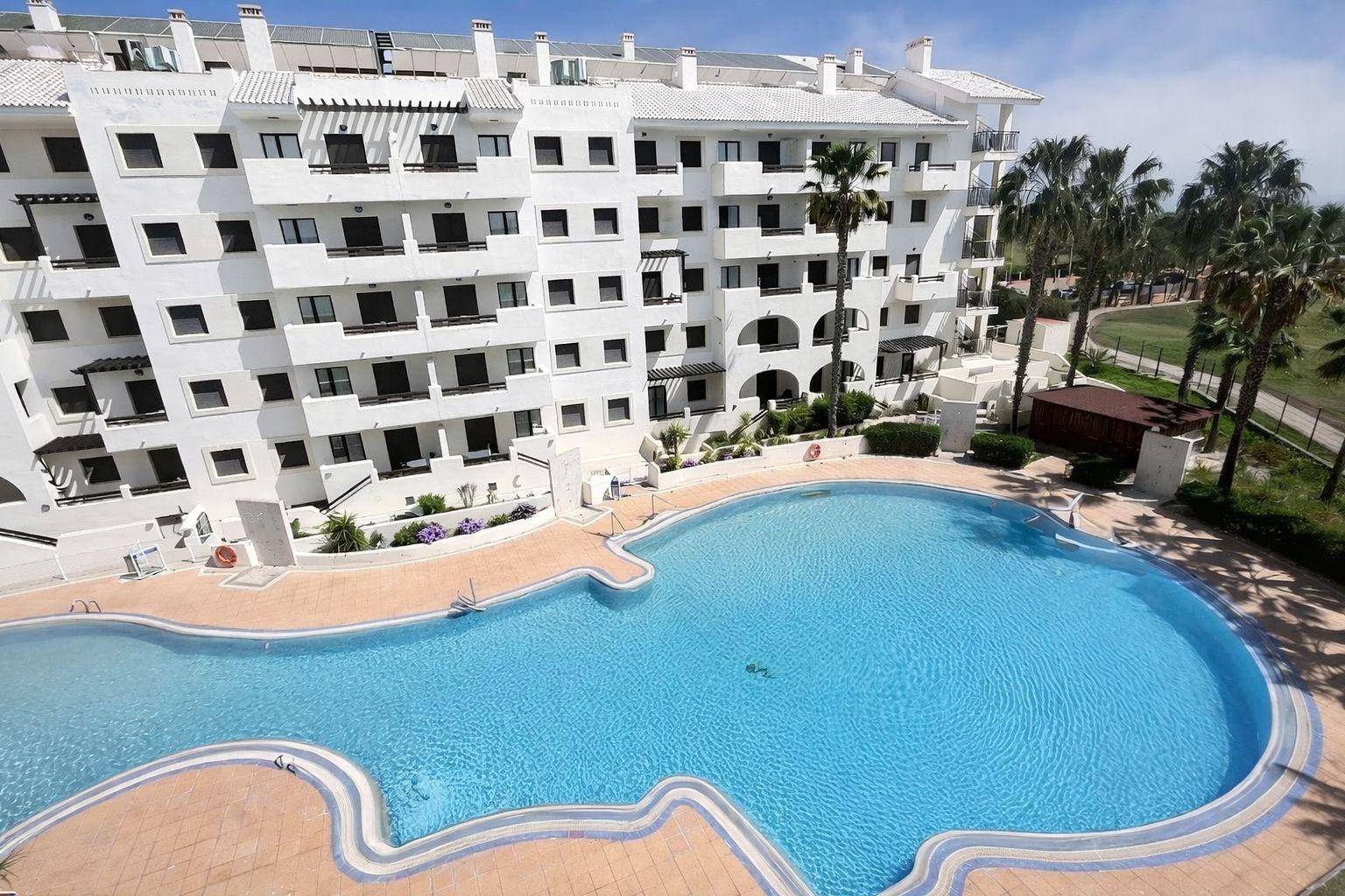 Weitläufige Apartmentanlage mit großem Poolbereich und umliegenden Palmen unter strahlendem Himmel.