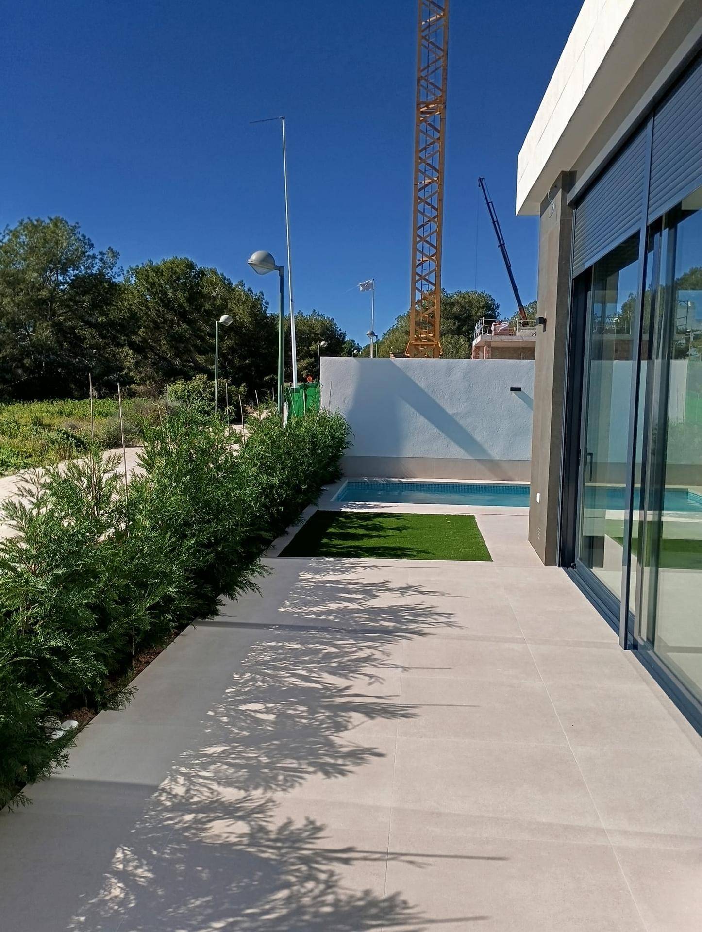 Außenbereich mit Pool, Rasenfläche und einem Baugelände im Hintergrund unter blauem Himmel.