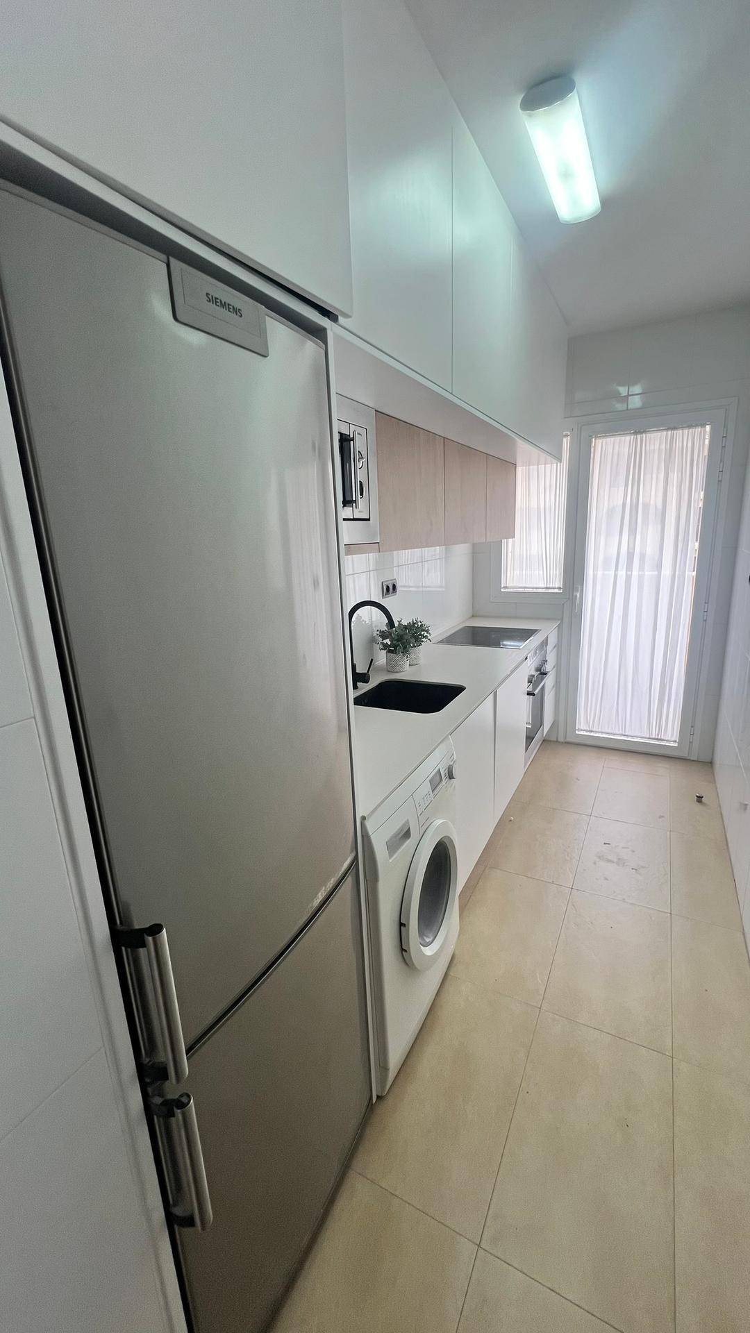 Moderne Einbauküche mit Kühlschrank, Waschmaschine und Holzdetails in hellem Design.
