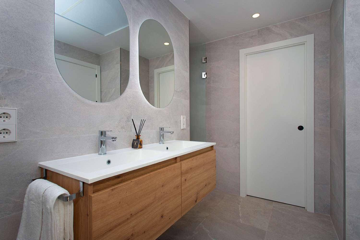 Modernes Badezimmer mit Doppelwaschbecken, Holzunterschrank und großen Spiegeln, sehr stilvoll.