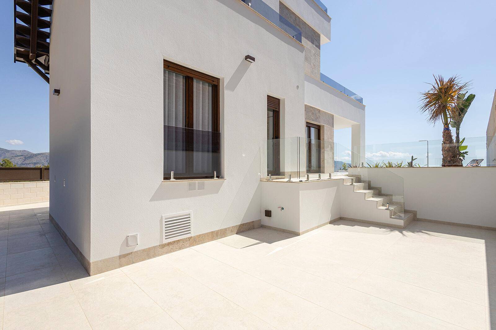 Seitlicher Außenbereich mit Fliesenboden, kleiner Terrasse und Blick auf Palmen und Meer.