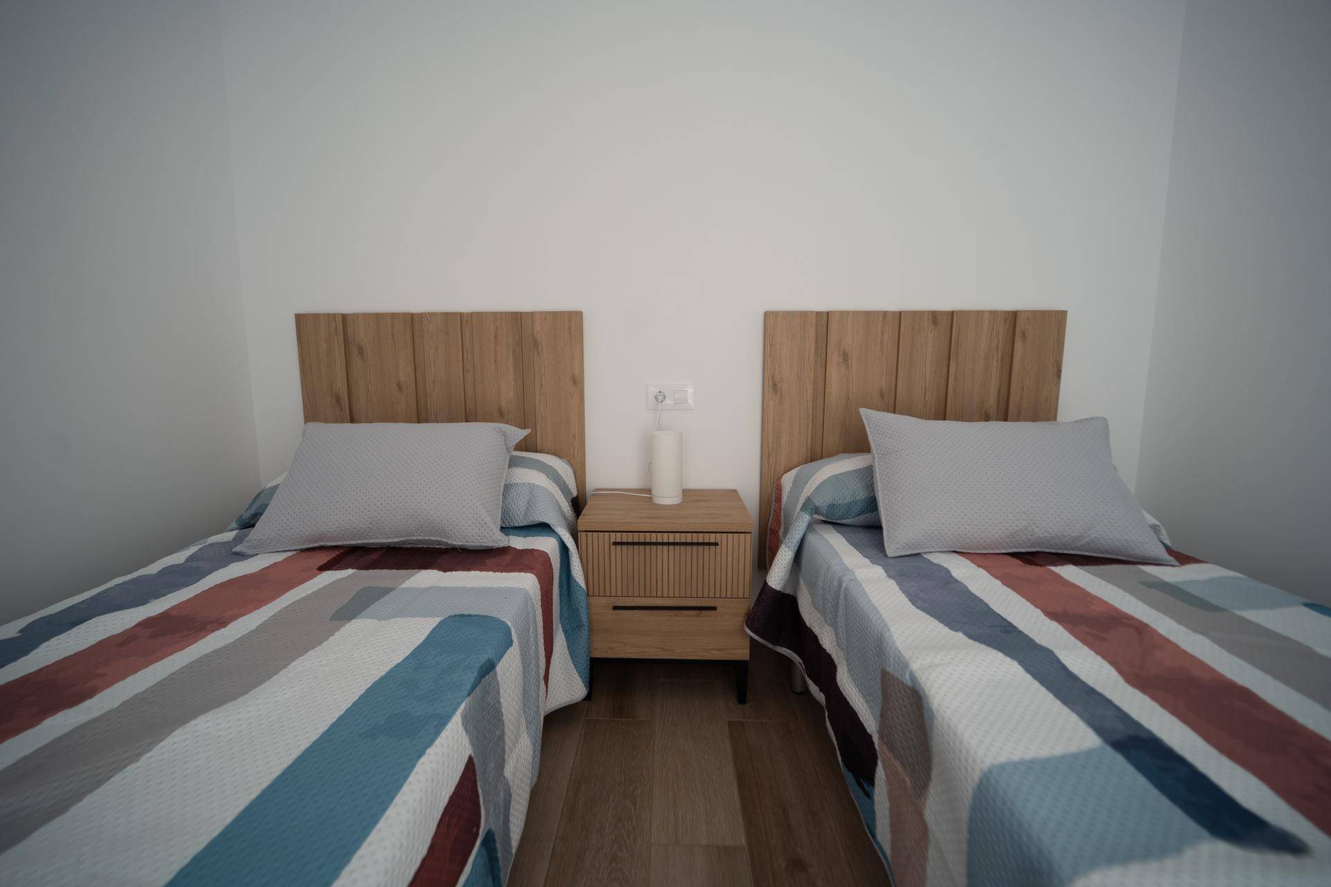 Helles Schlafzimmer mit zwei Einzelbetten, Holzkopfteilen und gestreiften Bettdecken.