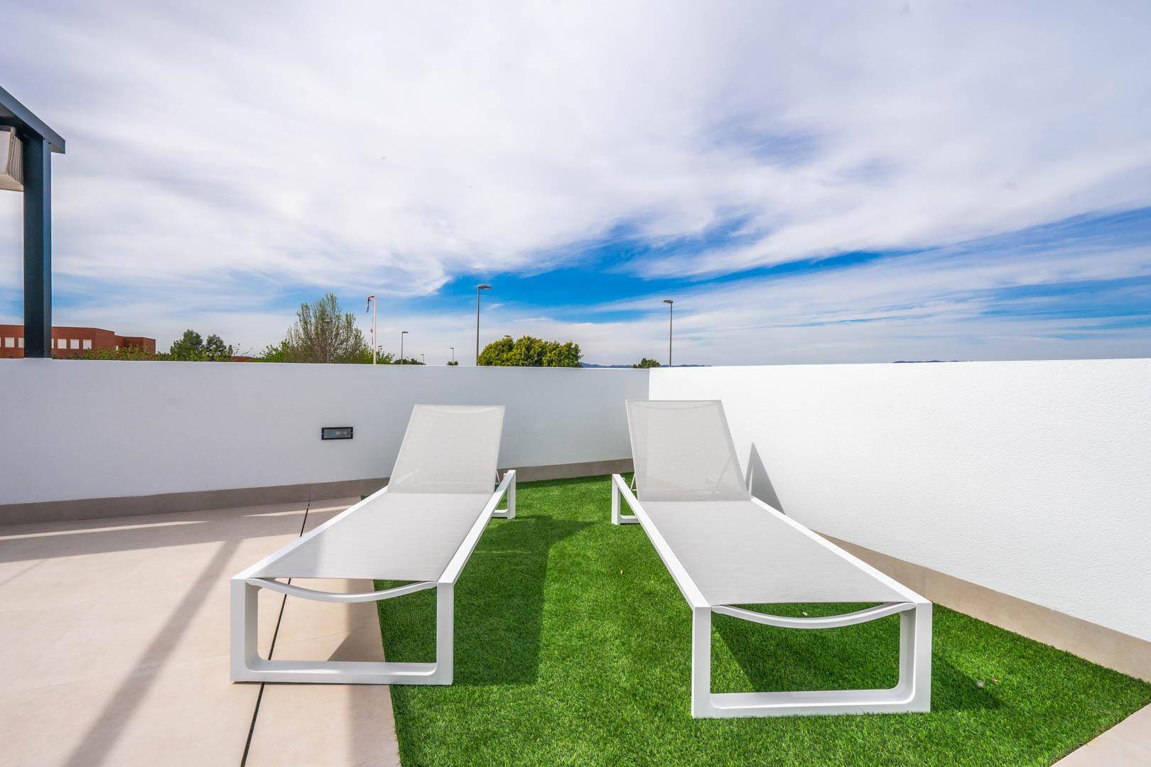 Sonnige Dachterrasse mit Liegestühlen und weitem Blick unter blauem Himmel.