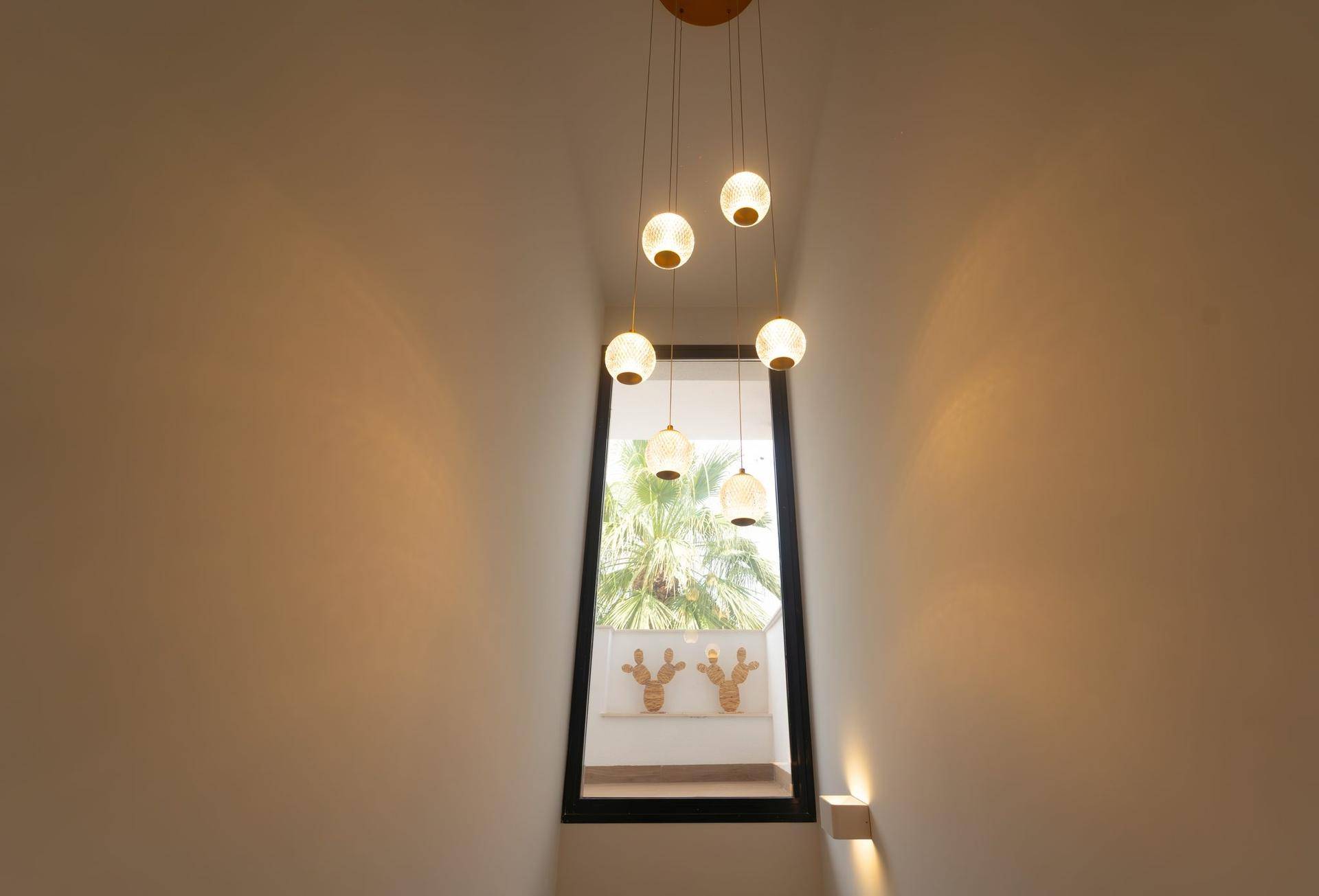 Treppenhaus mit moderner Hängeleuchte und Fenster, das viel natürliches Licht hereinlässt.