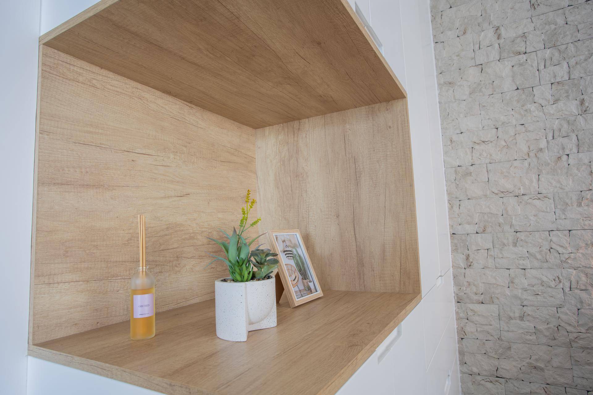 Dekorative Holznische mit Pflanze und Bilderrahmen neben einer strukturierten Steinwand.