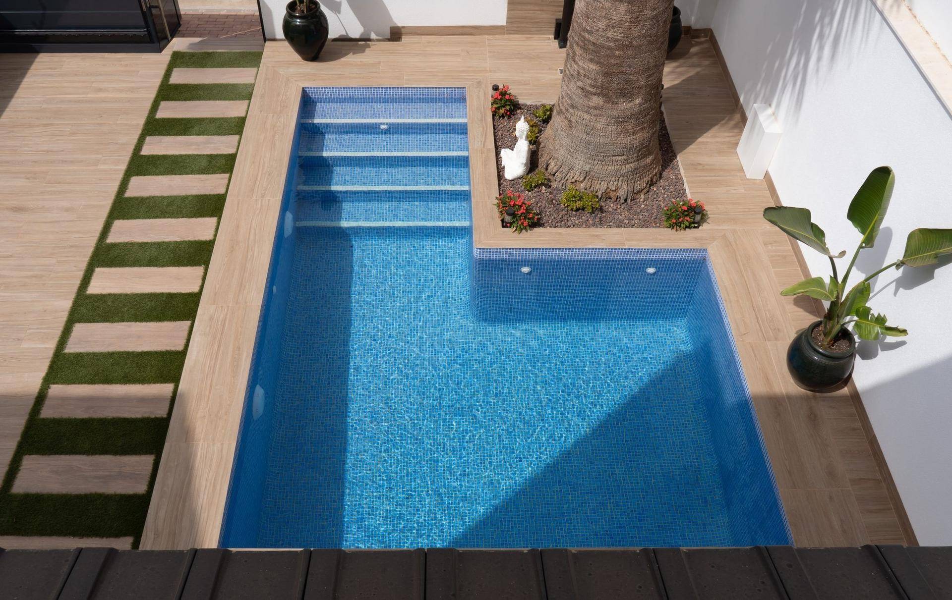 Kleiner privater Poolbereich mit Holzdeck, Kunstrasen und einer Palme im Zentrum.