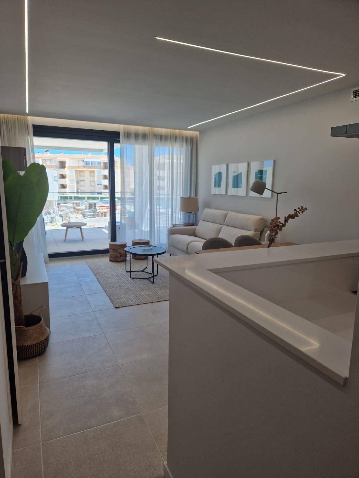 Heller Wohnbereich mit Sofa, Couchtischen und Zugang zum Balkon durch große Fenster.