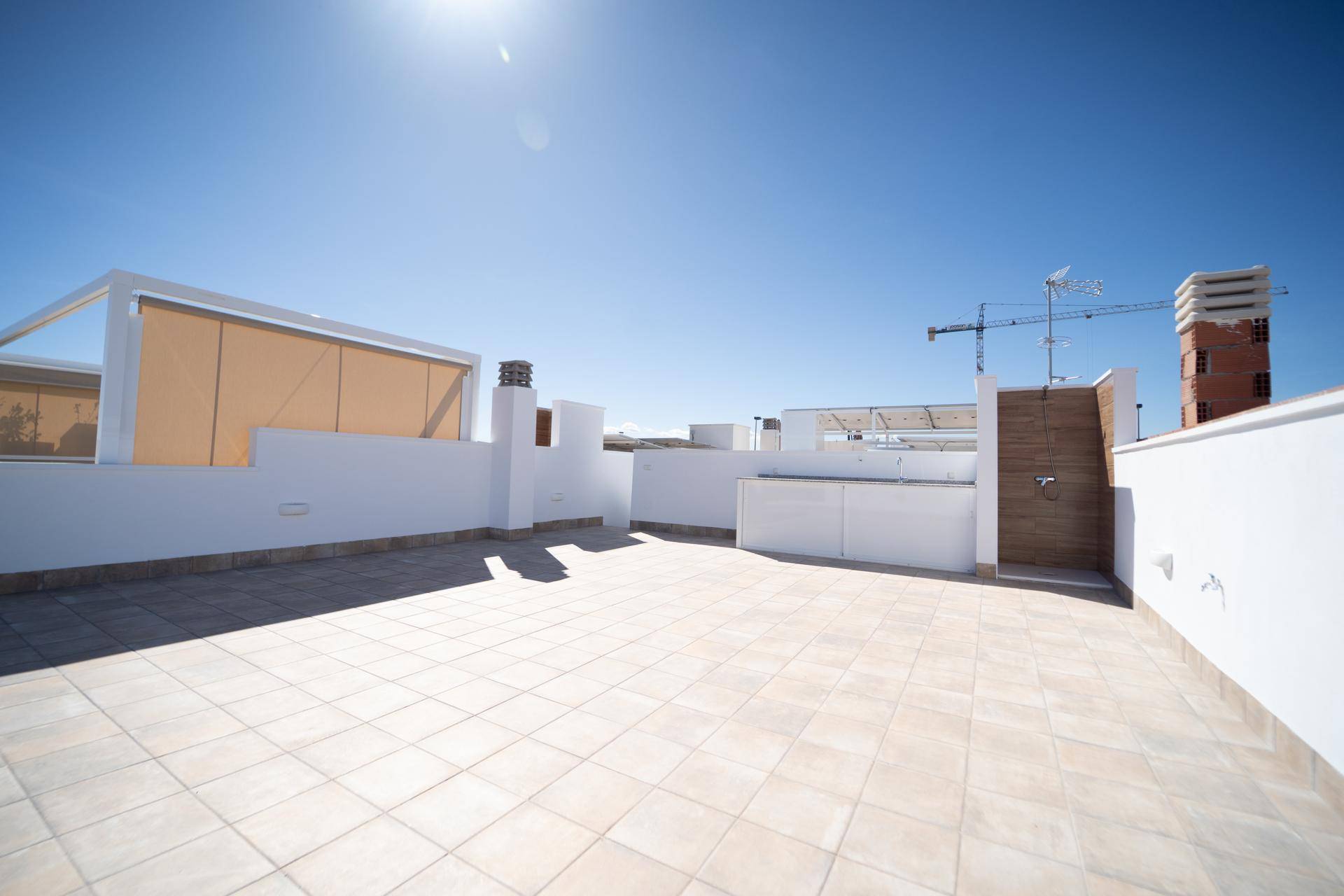 Sonnige Dachterrasse mit Fliesenboden und Blick auf die Umgebung und eine Baustelle.