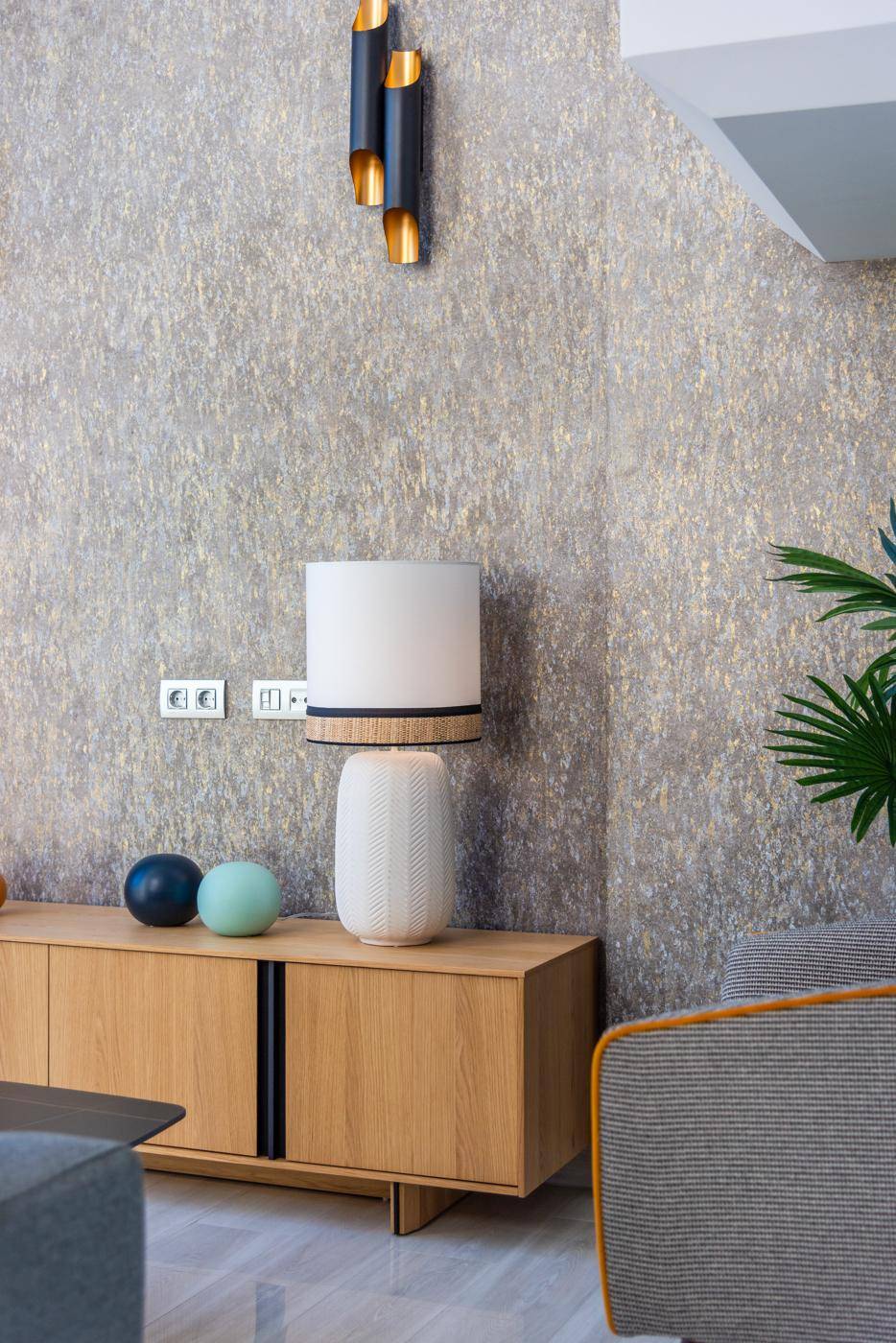 Detailansicht des Wohnzimmers mit modernem Sideboard, Tischlampe und strukturierter Wand.