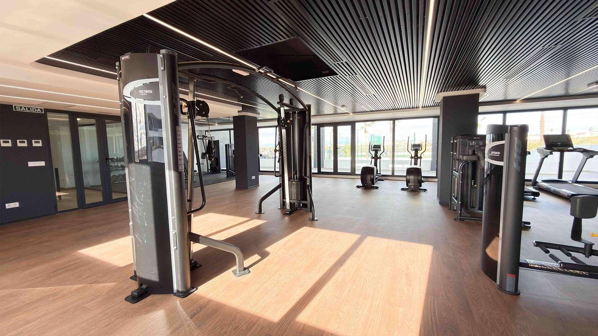 Moderner Fitnessraum mit verschiedenen Trainingsgeräten und großen Fenstern für natürliches Licht.