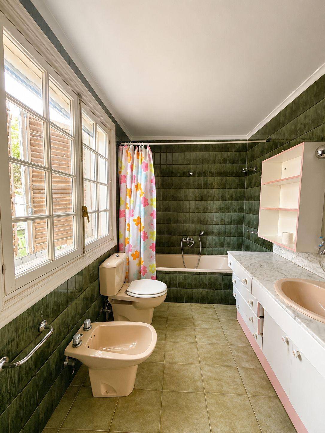 Badezimmer mit grünen Fliesen, rosa Sanitärobjekten, Badewanne und Fenster für Tageslicht.