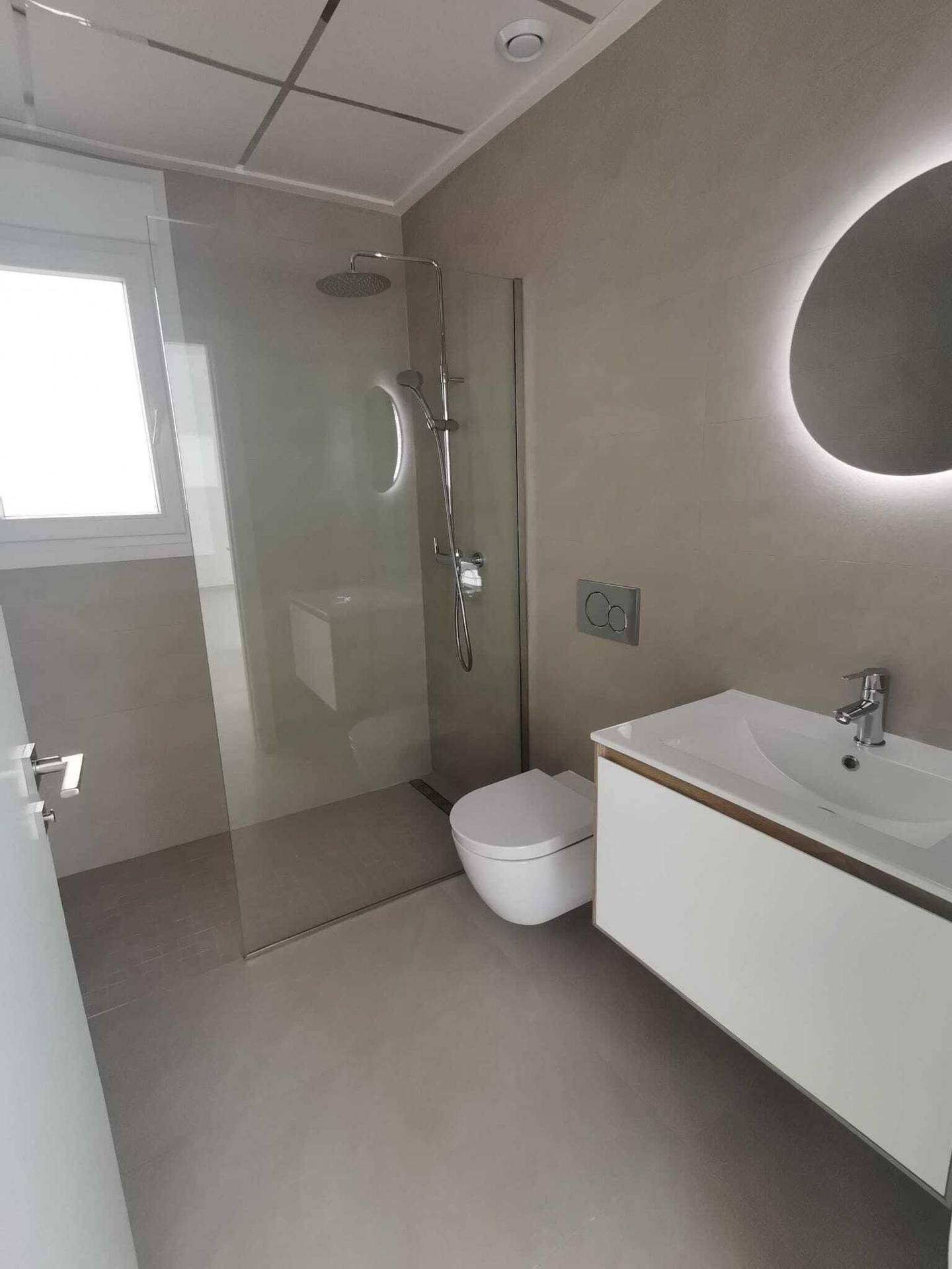 Modernes Badezimmer mit begehbarer Dusche, schwebendem Waschtisch und beleuchtetem Spiegel.