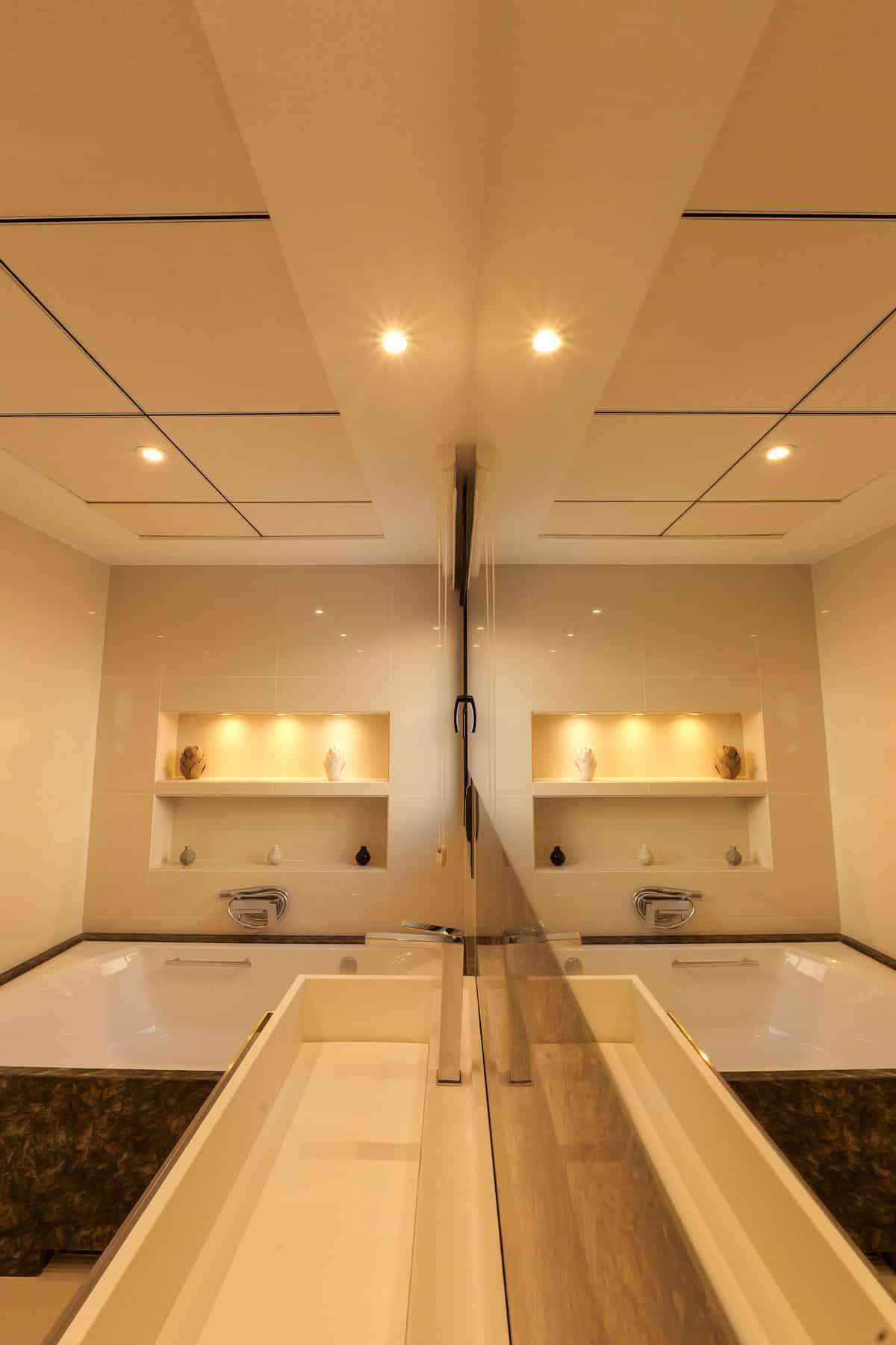 Elegantes Badezimmer mit integrierter Badewanne, Spiegelflächen und indirekter Beleuchtung.