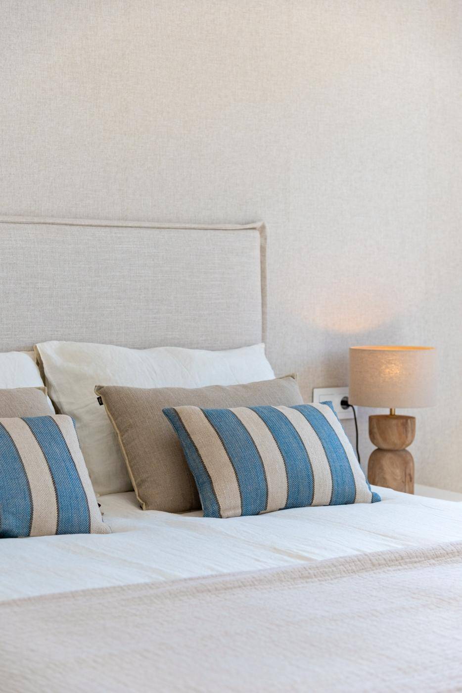Nahaufnahme eines Bettes mit gestreiften Kissen und einer Nachttischlampe in einem hellen Schlafzimmer.