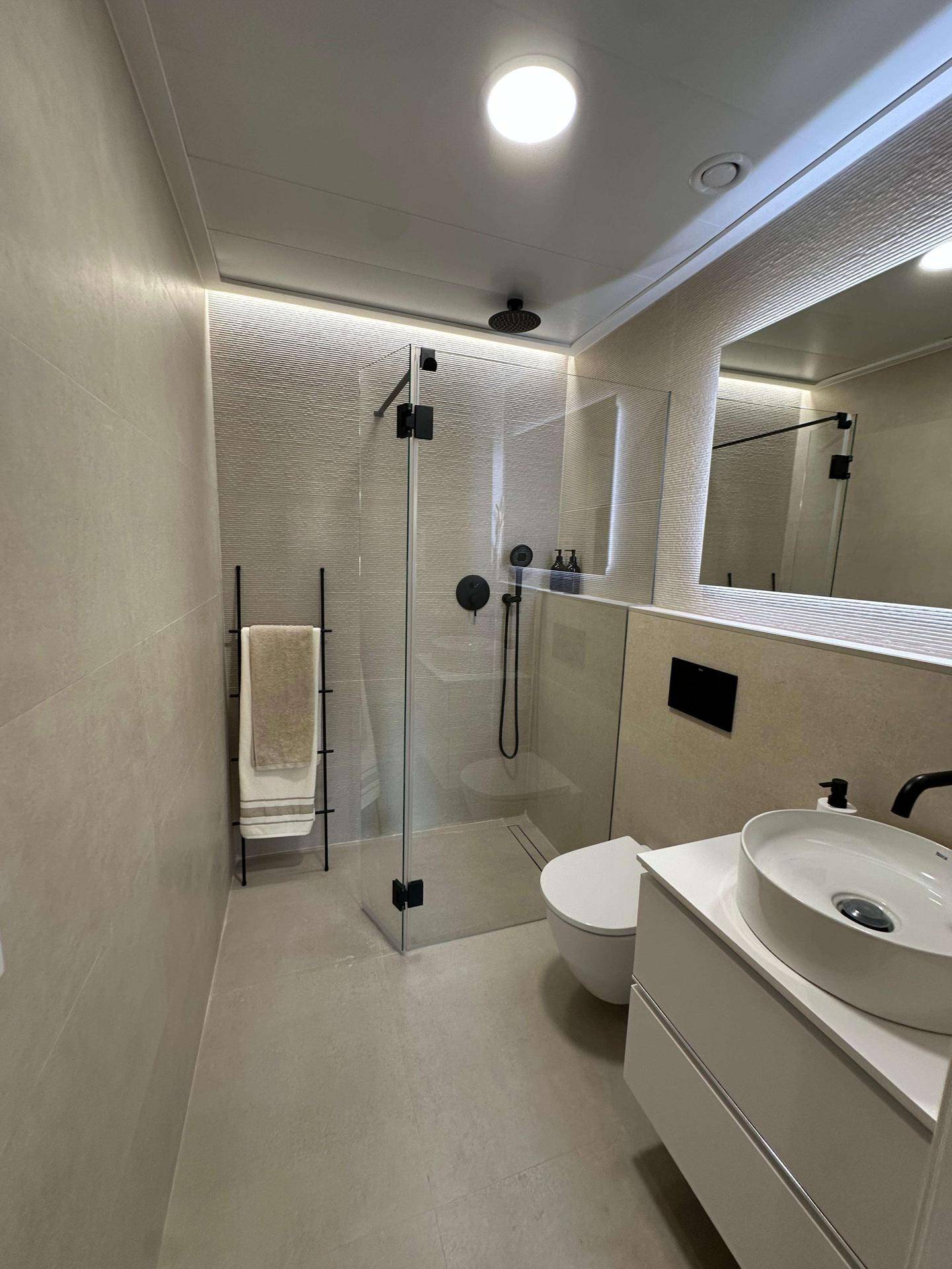 Modernes Badezimmer mit begehbarer Dusche, Wand-WC und beleuchtetem Spiegel.