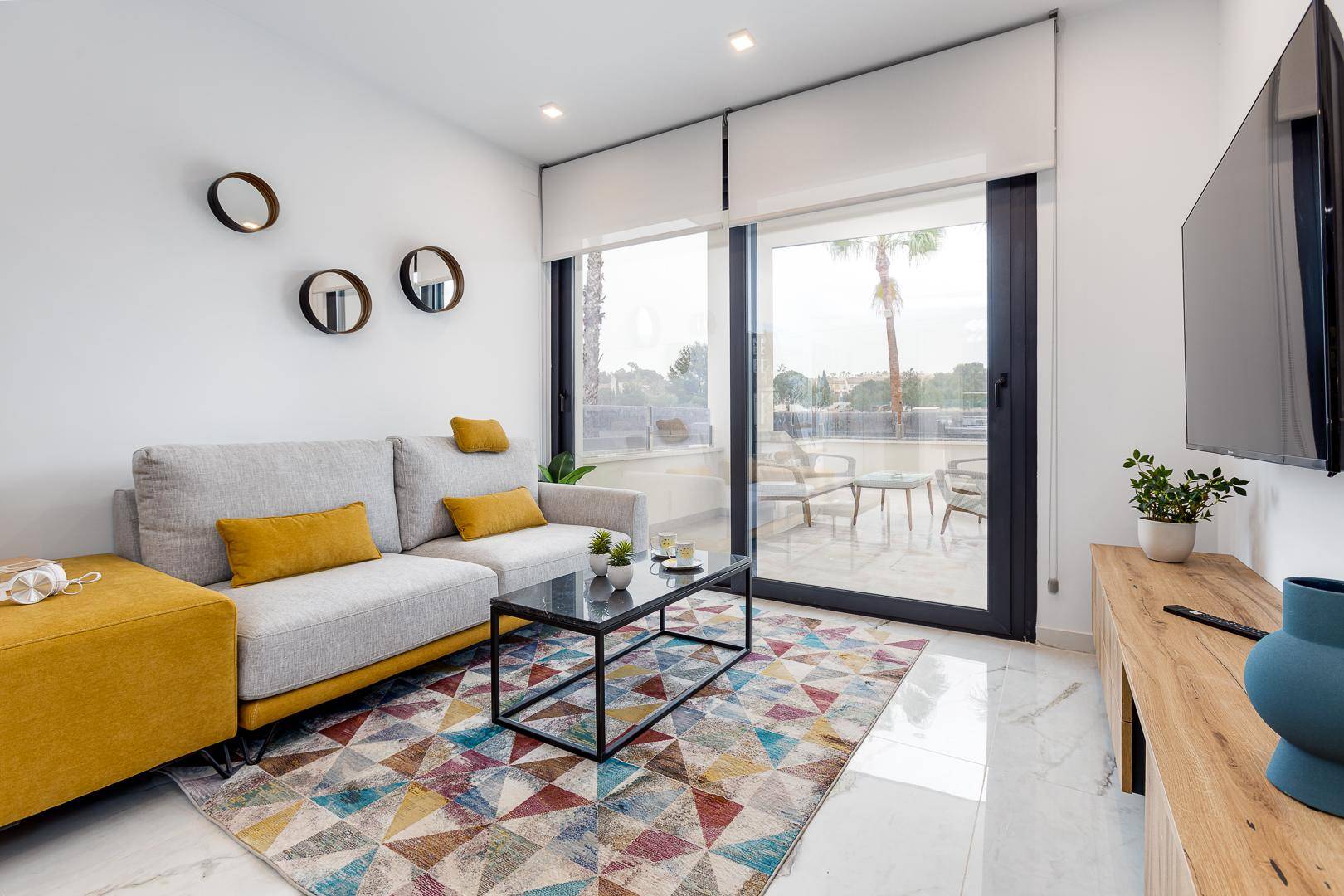 Helles Wohnzimmer mit modernem Sofa, farbenfrohem Teppich und Zugang zur Terrasse.