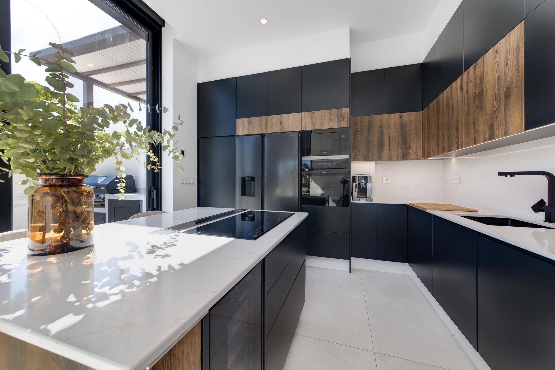 Moderne Küche mit dunklen Schränken, Holzdetails und heller Arbeitsplatte, mit Zugang zur Terrasse.